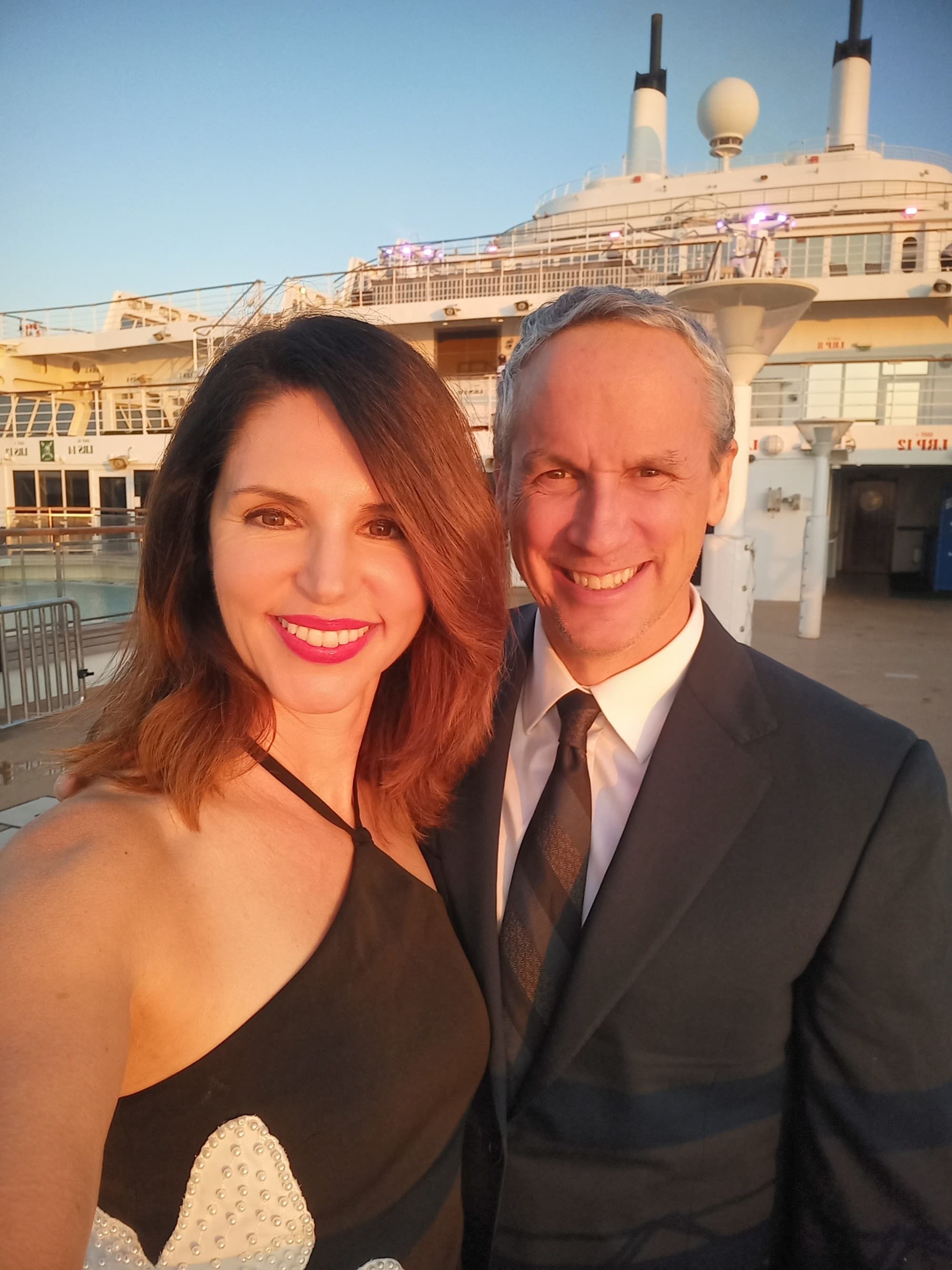 A couple posing in front of a cruise ship in formal wear.