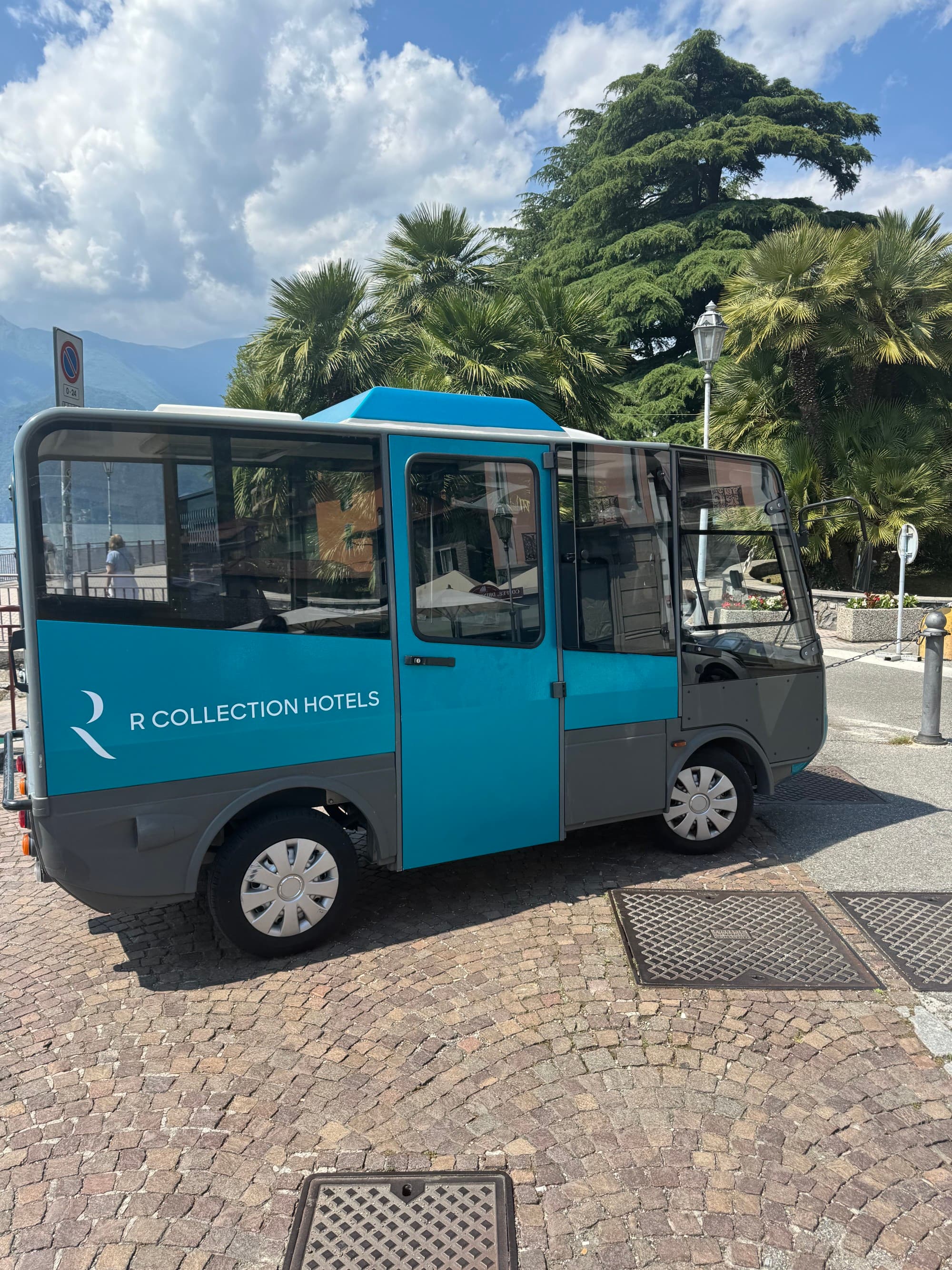 Hotel Royal Victoria Minivan that is teal blue and grey with the words "R Collection Hotels" written in white on the side