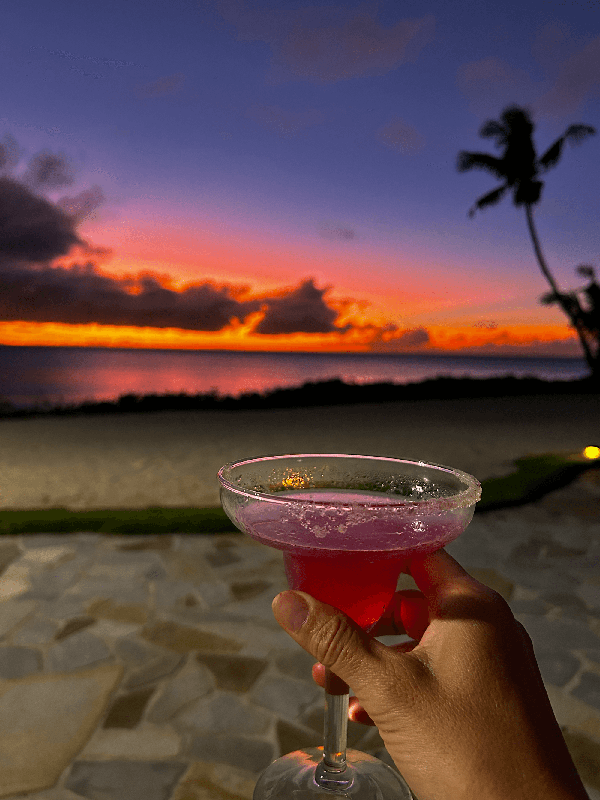 A person holding a drink in a cocktail glass on the beach during the sunset