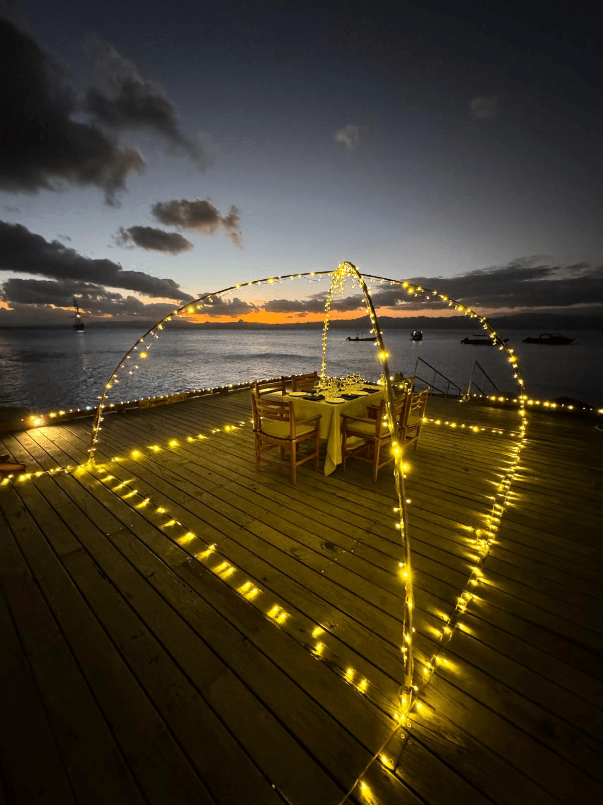 A dining set up on a deck with warm yellow string lighting above and around the table.