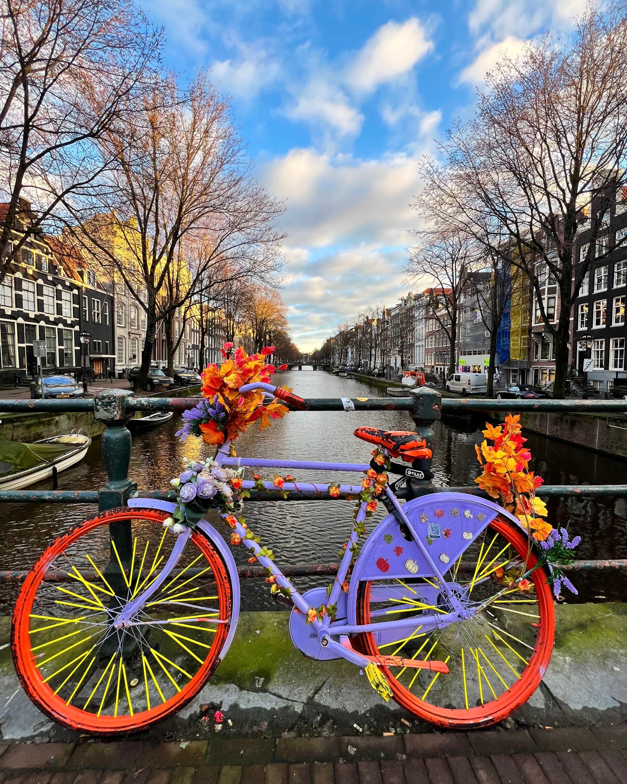 A bright, iconic bicycle perches against the railing over a canal on a clear day dotted with clouds.