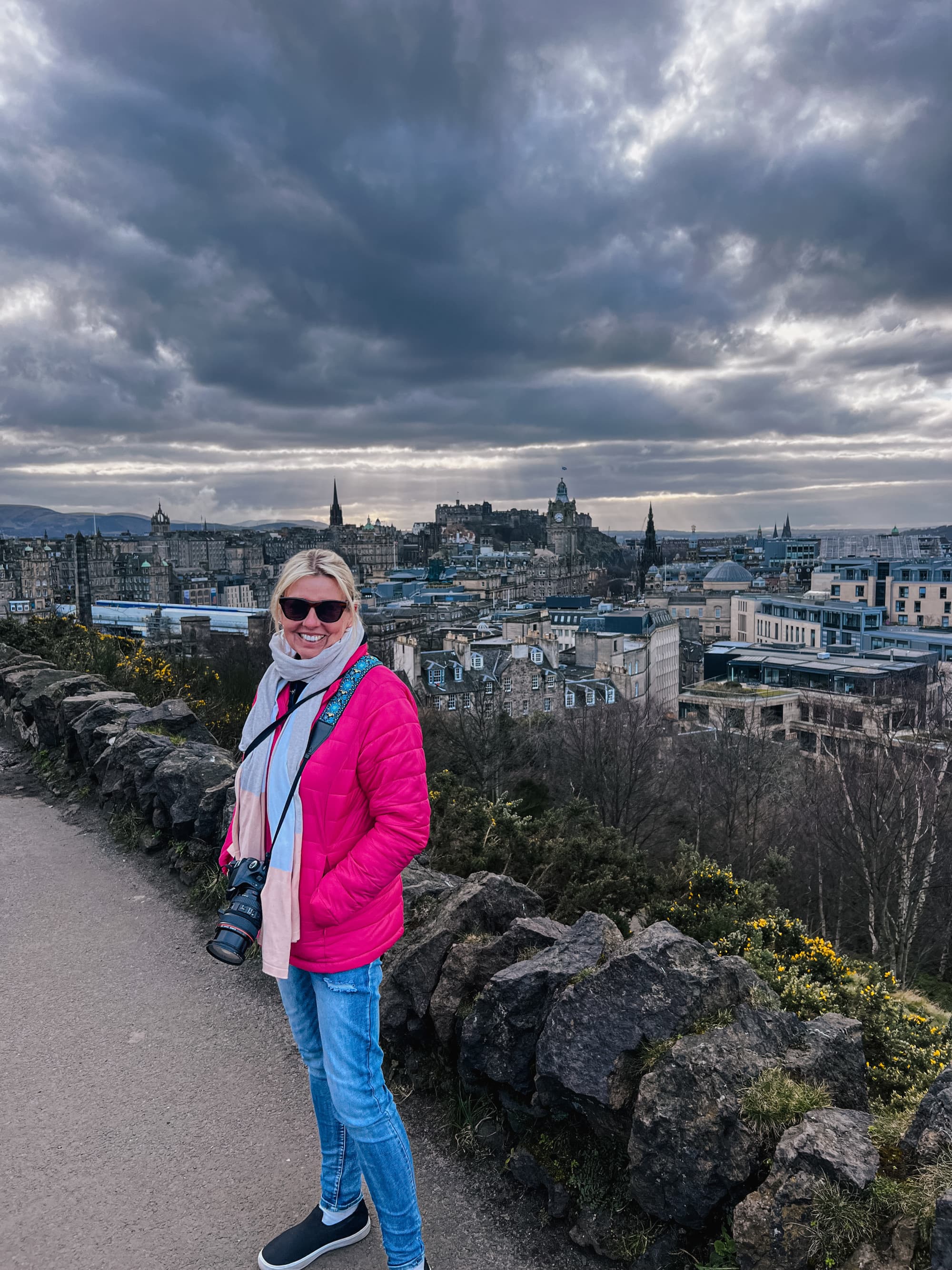 Advisor posing on a hilltop overlooking Edinburgh under a cloudy sky.