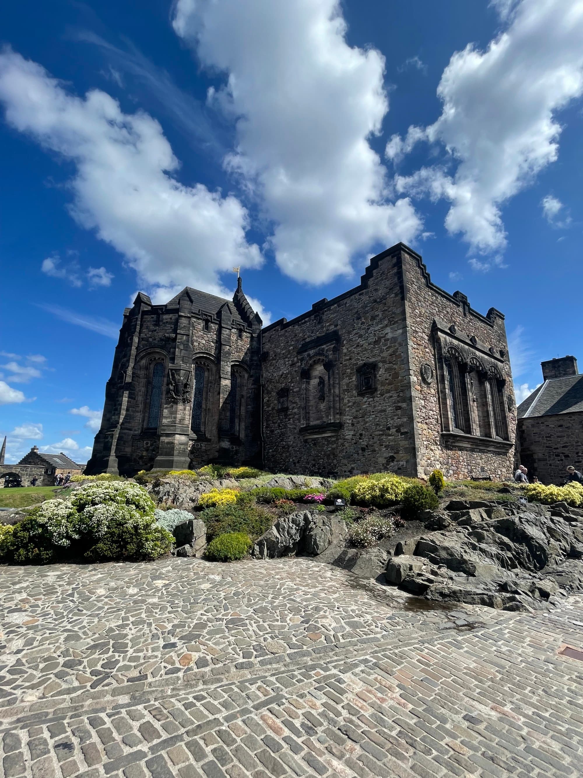 A coble stone street in front of a large Old Castle in Edinburgh during the day.