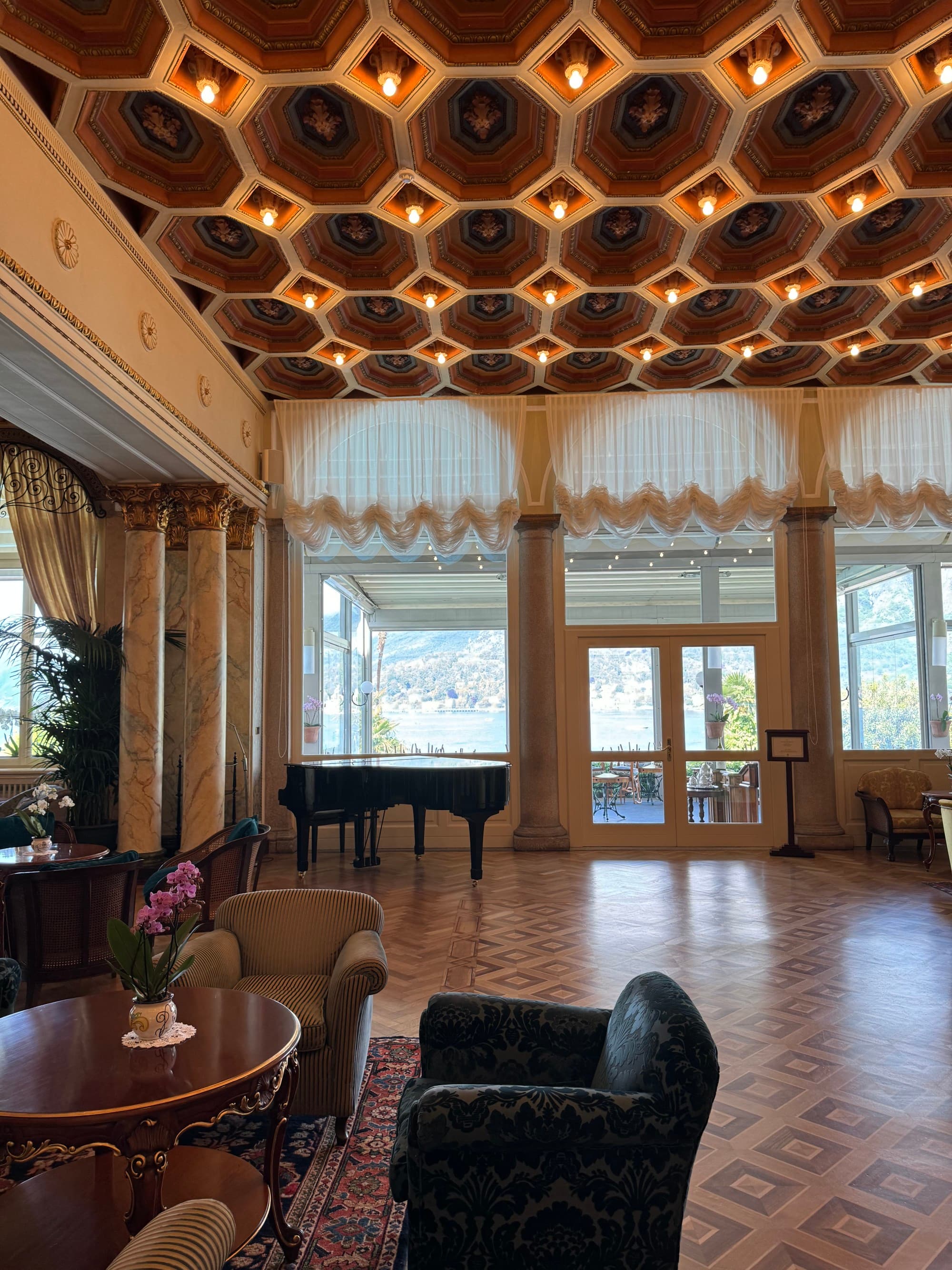 Lounge interior with sun spilling through the windows with a grand piano in the corner.