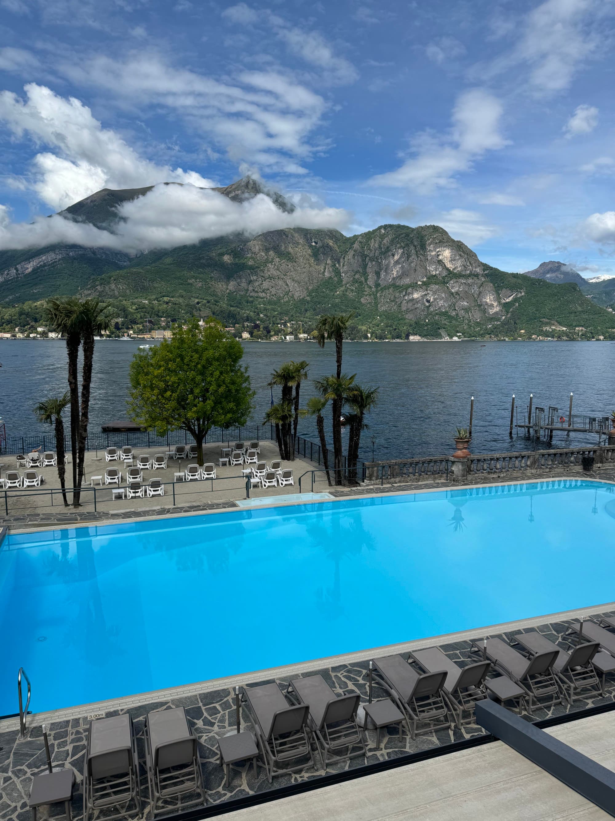 Pool and poolside view overlooking a mountainside on a sunny day dotted with clouds.