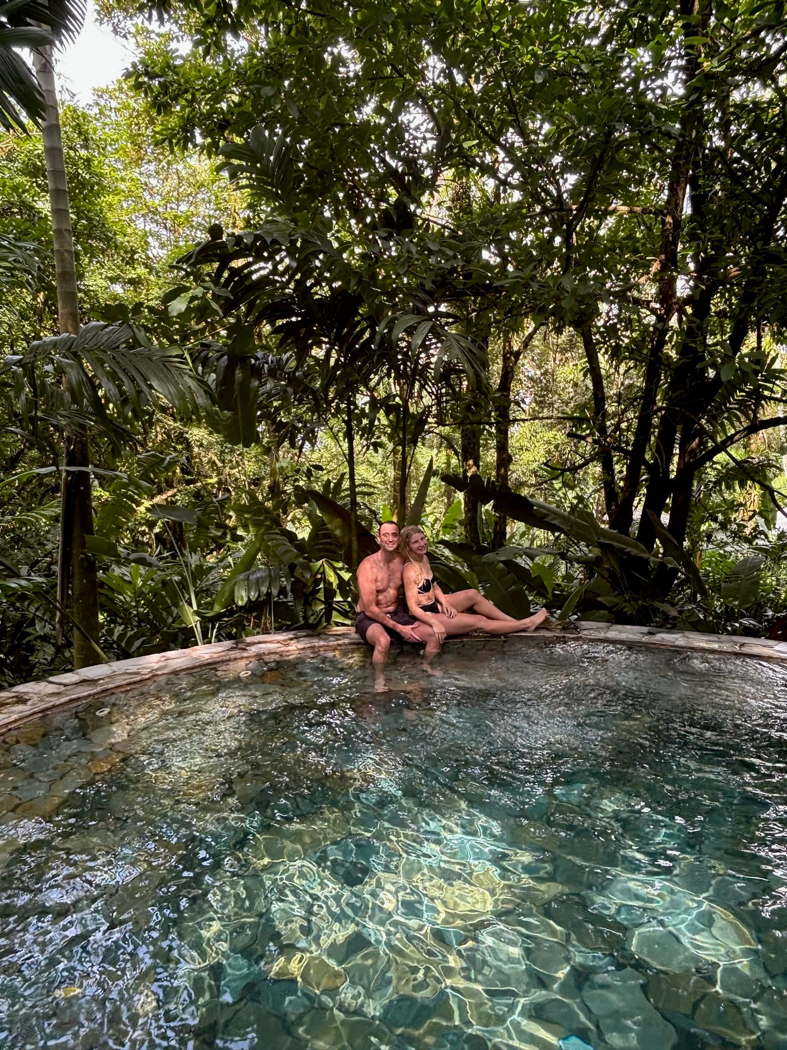 Couple sitting in hot springs with jungle in the background.