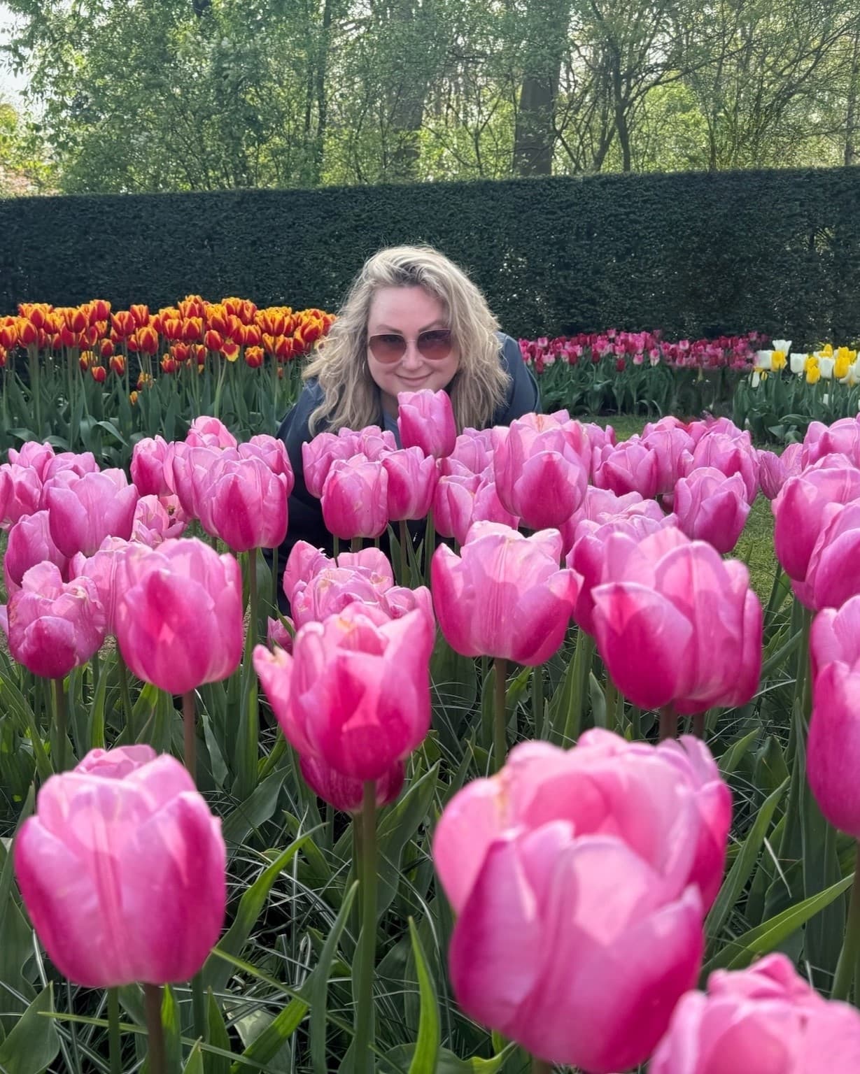 Advisor posing in a garden full of pink tulips with red, pink and yellow tulips behind her in the Keukenhof Garden, Amsterdam