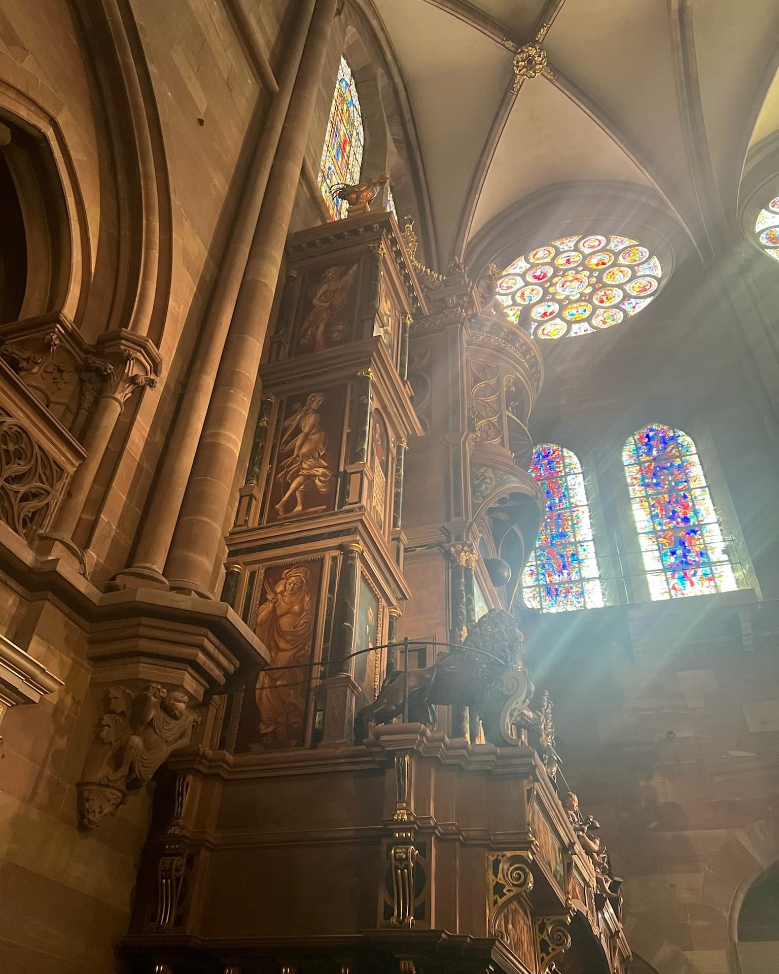 A view of a giant historical clock called the Astronomical clock at Strausburg Cathedral with an arched ceiling, stained glass windows and skylights around it.