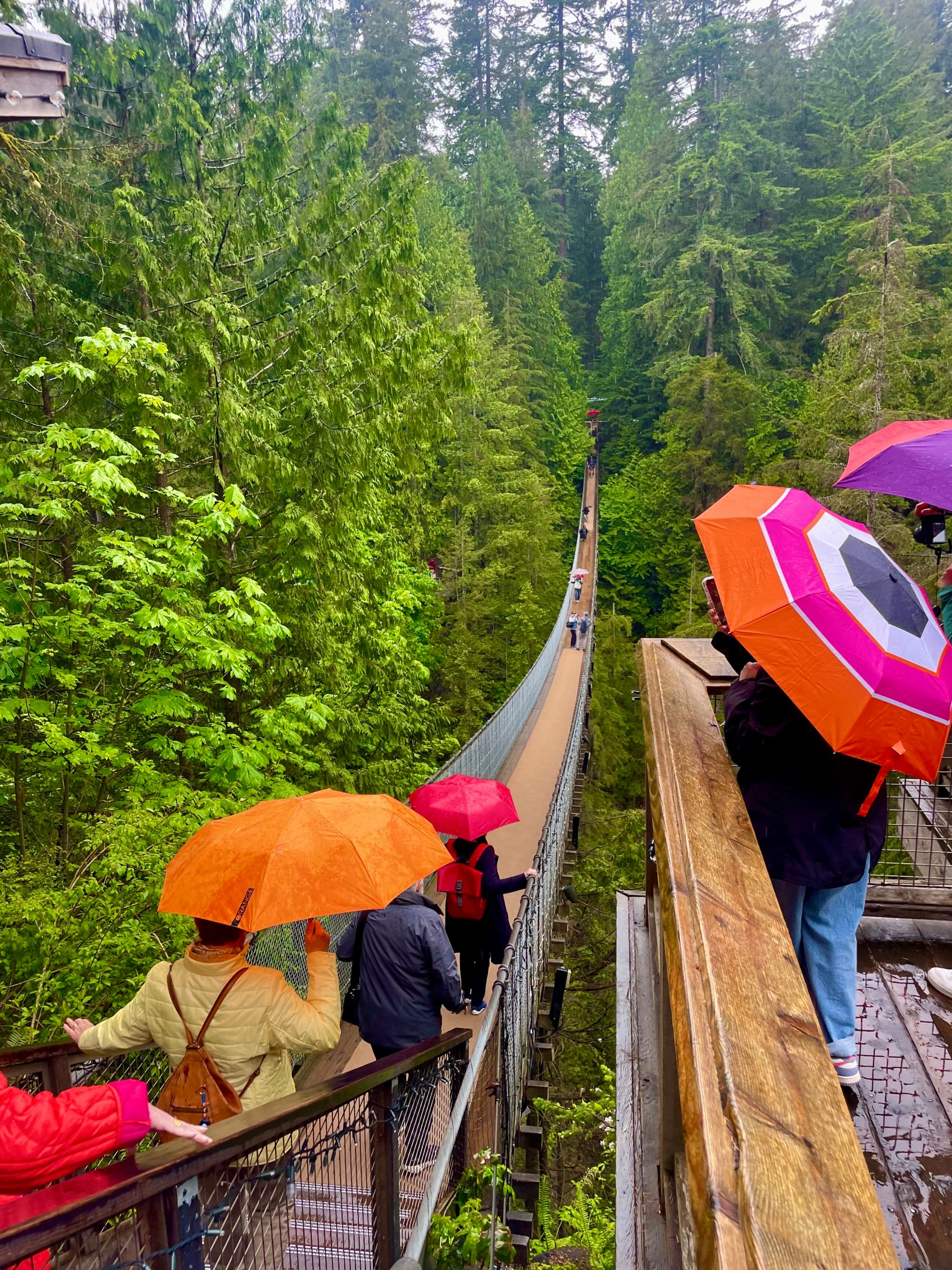 People crossing a bridge with colorful umbrellas.