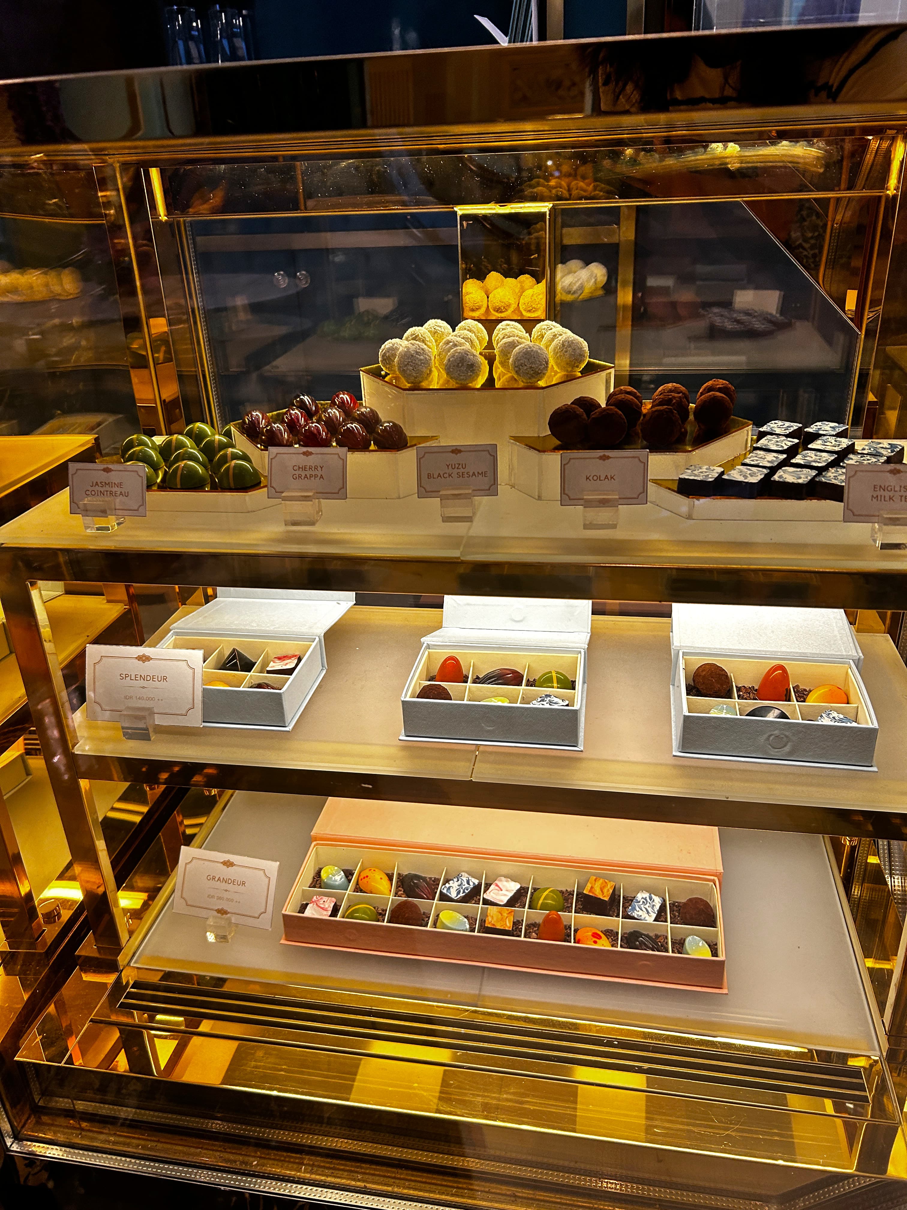 A glass cabinet display of boxes of sweet assortments at a store.