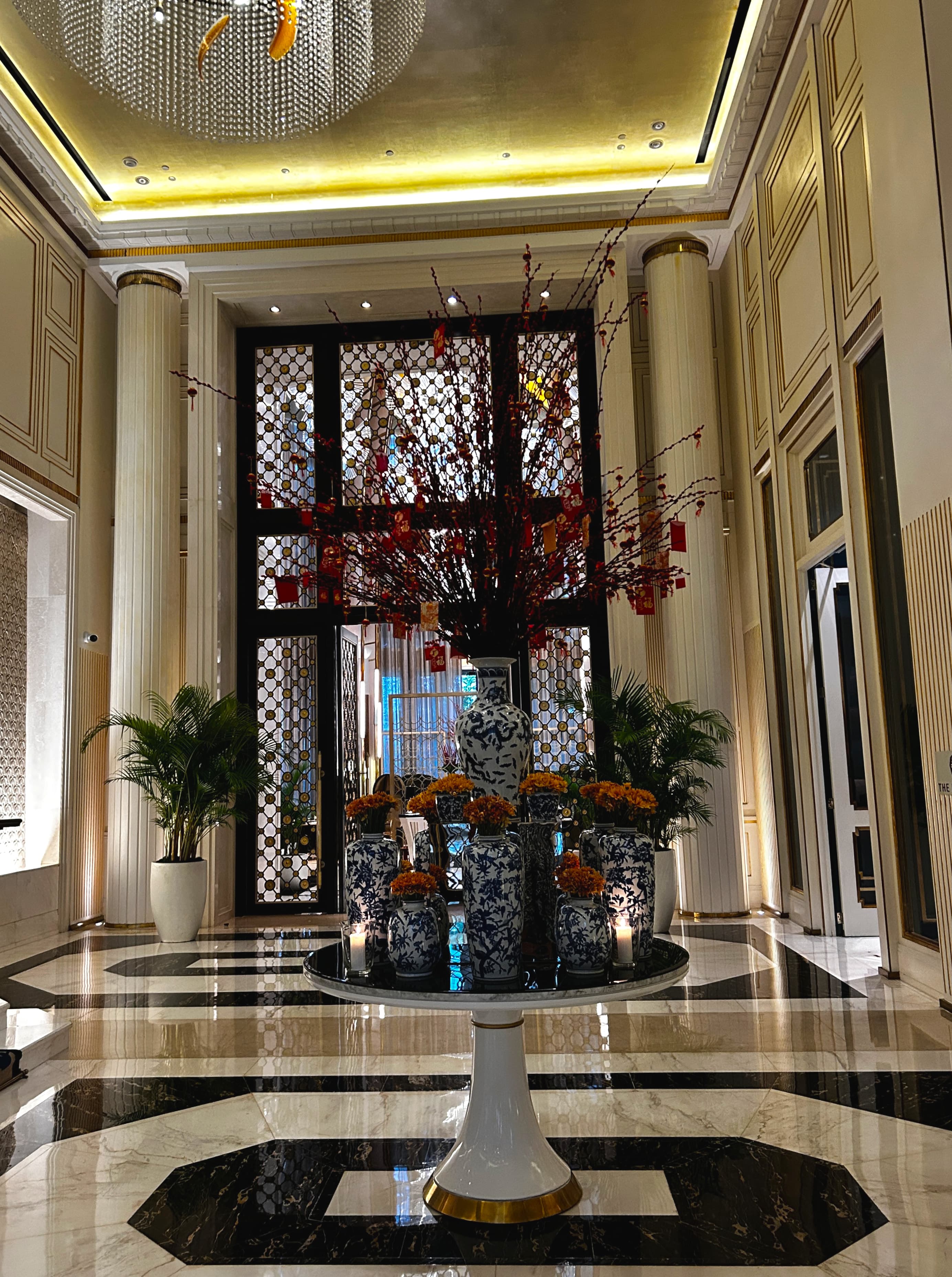 A grand lobby area with high ceilings, pillar, marble flooring and a central floral arrangement.