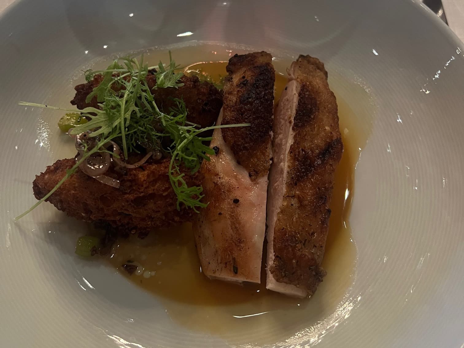 Chicken breast on a white plate with greens and yellow sauce.