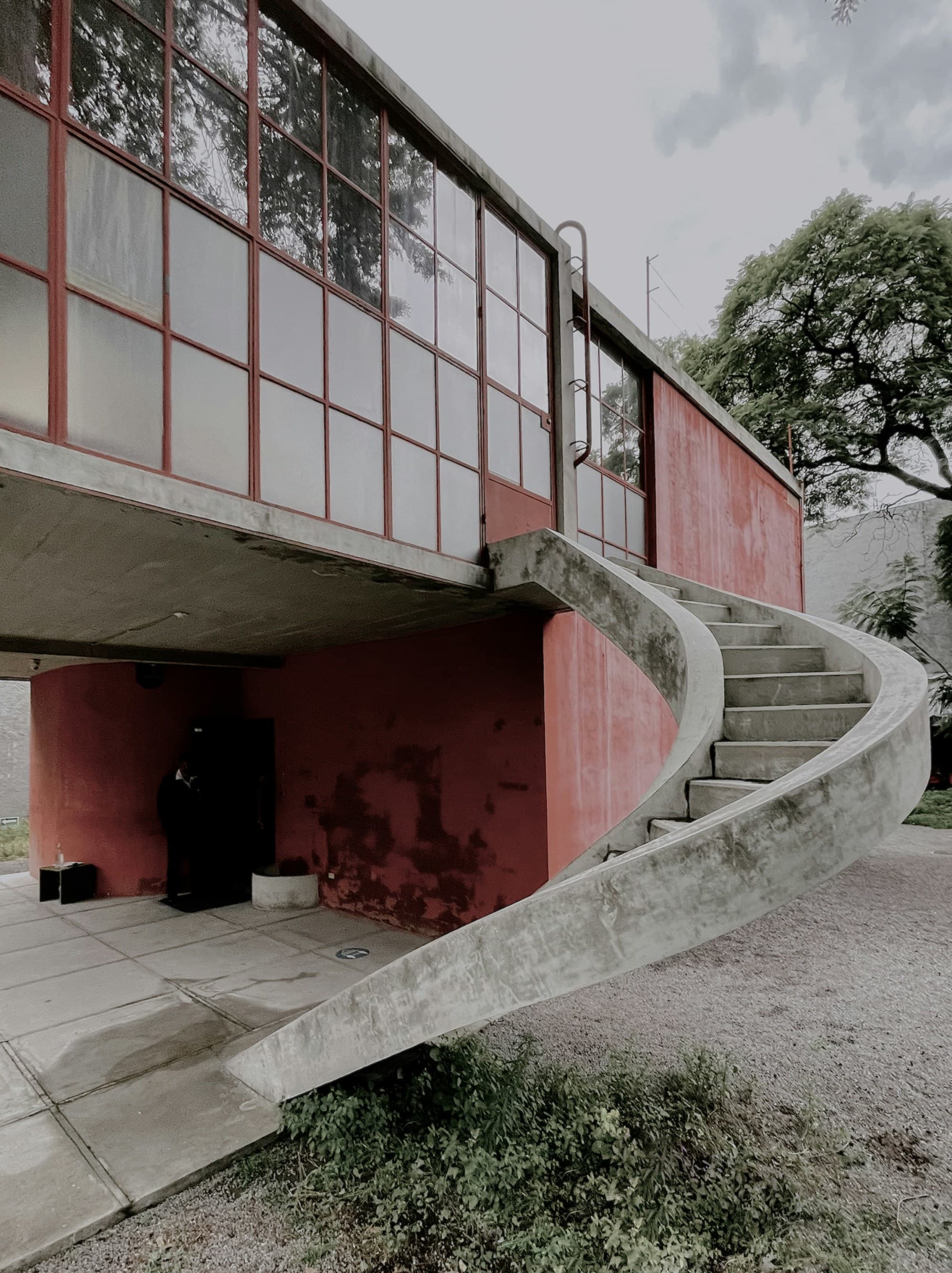 the exterior of a red building with a window wall and a spiral concrete staircase