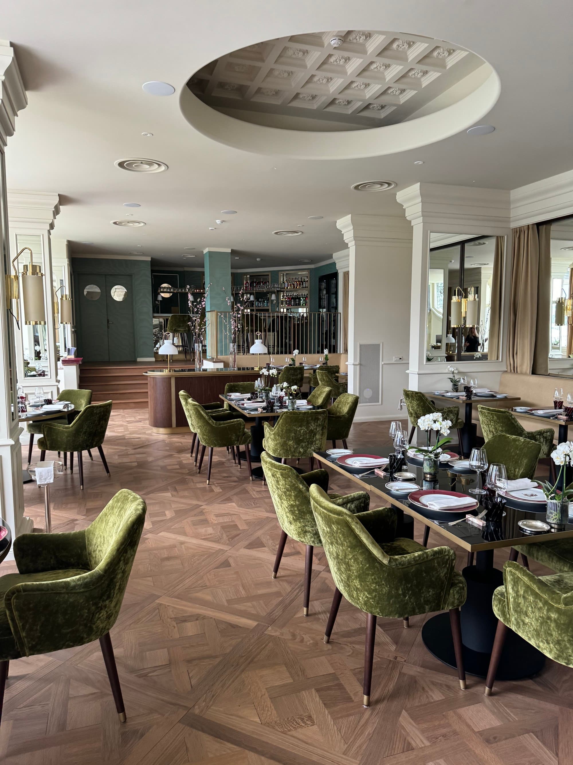 A dining area with vintage charm decorated with a blue accent wall behind the bar, wooden tables and olive green chairs.