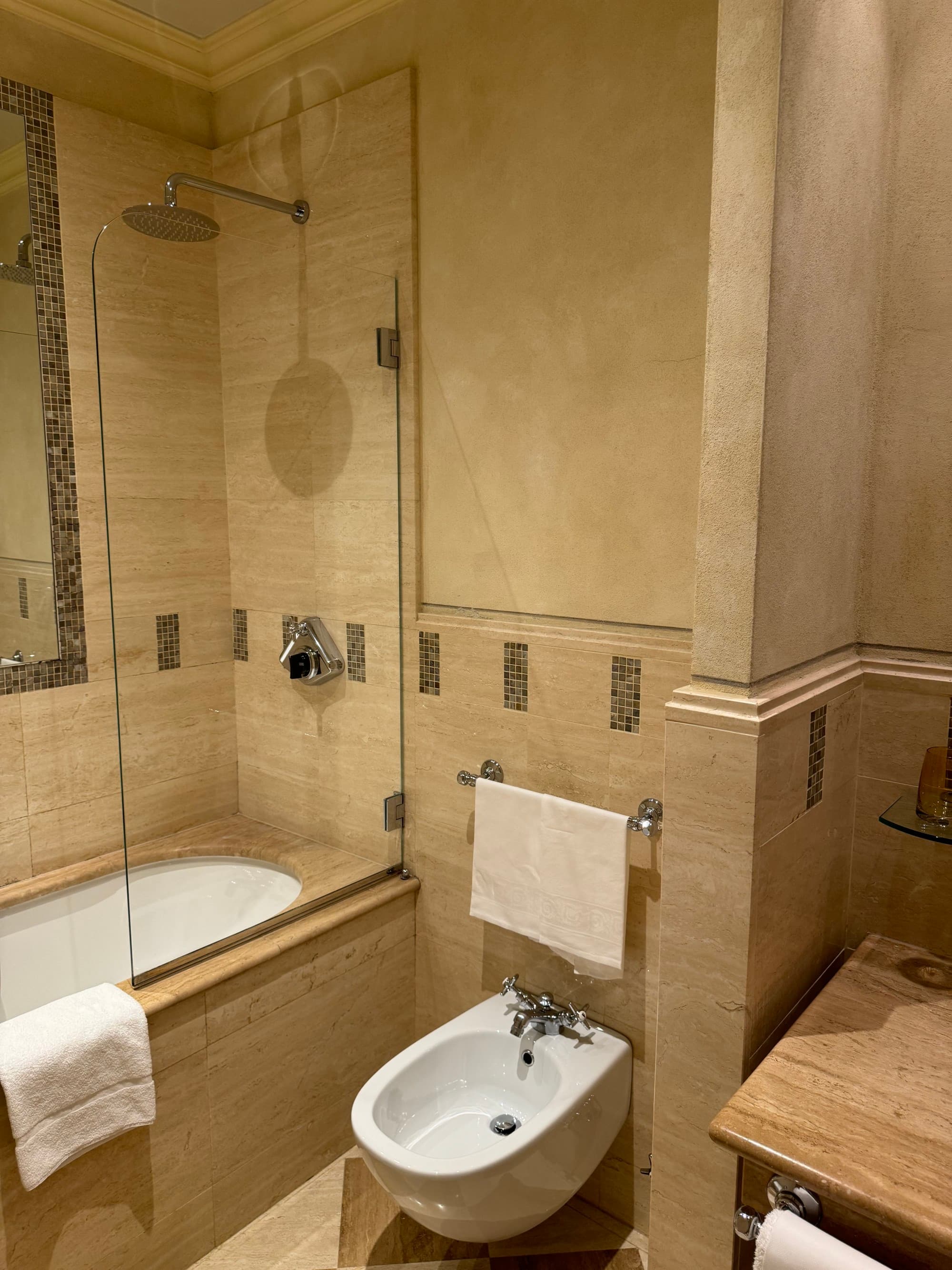 A tan tiled bathroom with a bidet and bathtub.