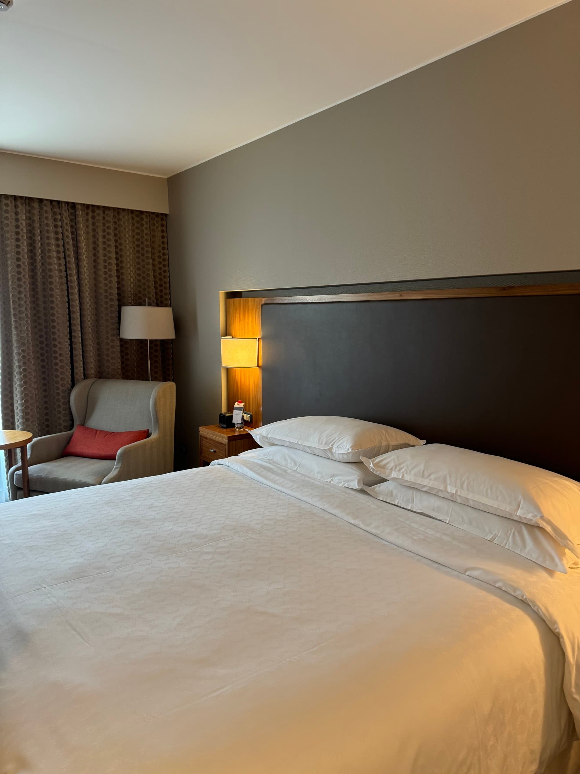 A photo of a white linen hotel bed with a lounge chair in the corner.