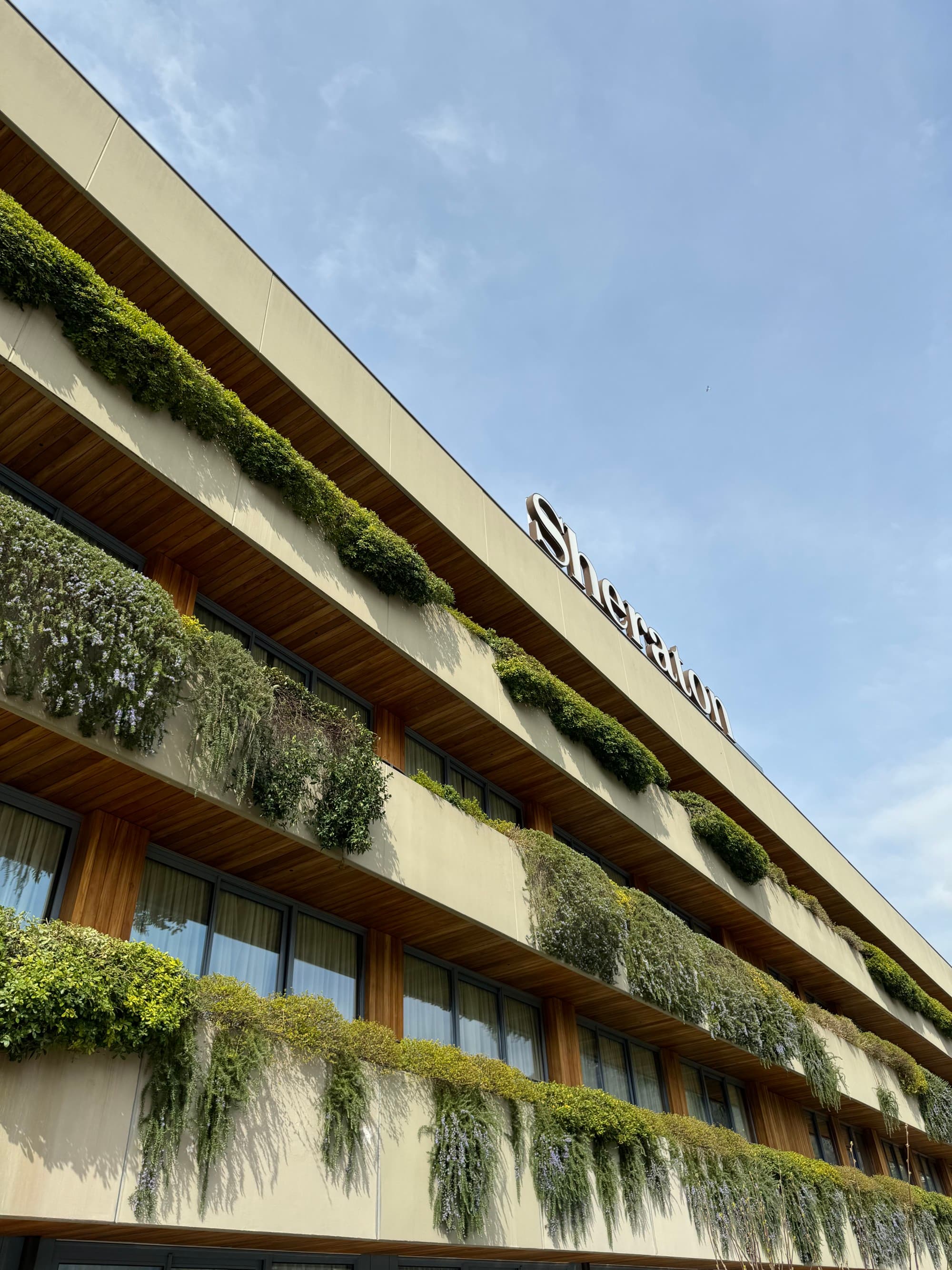 A photo of the front of the Sheraton from the ground with plants hanging from each of the room balconies.