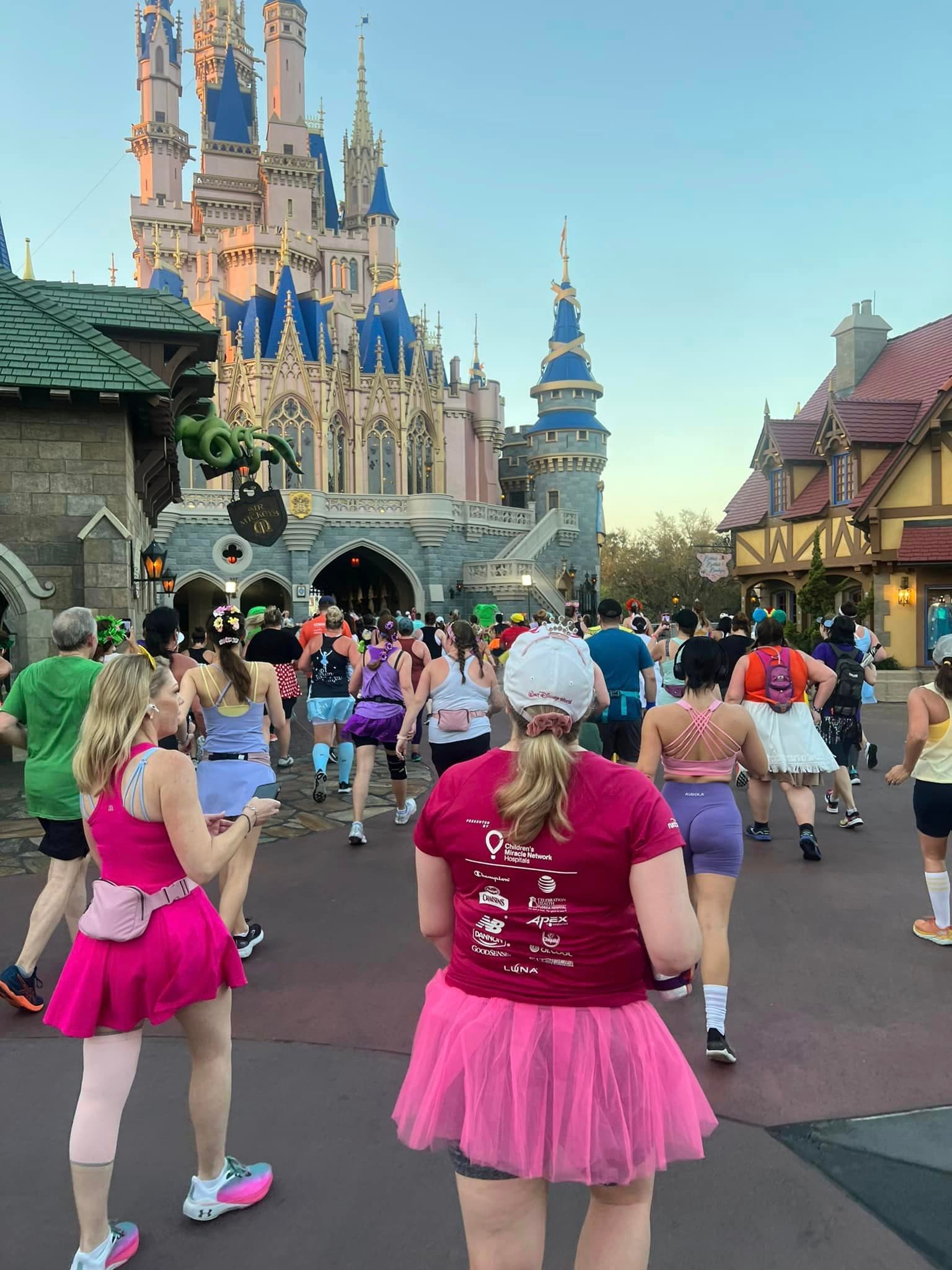 A group of people running through a Disney park in front of the iconic castle structure