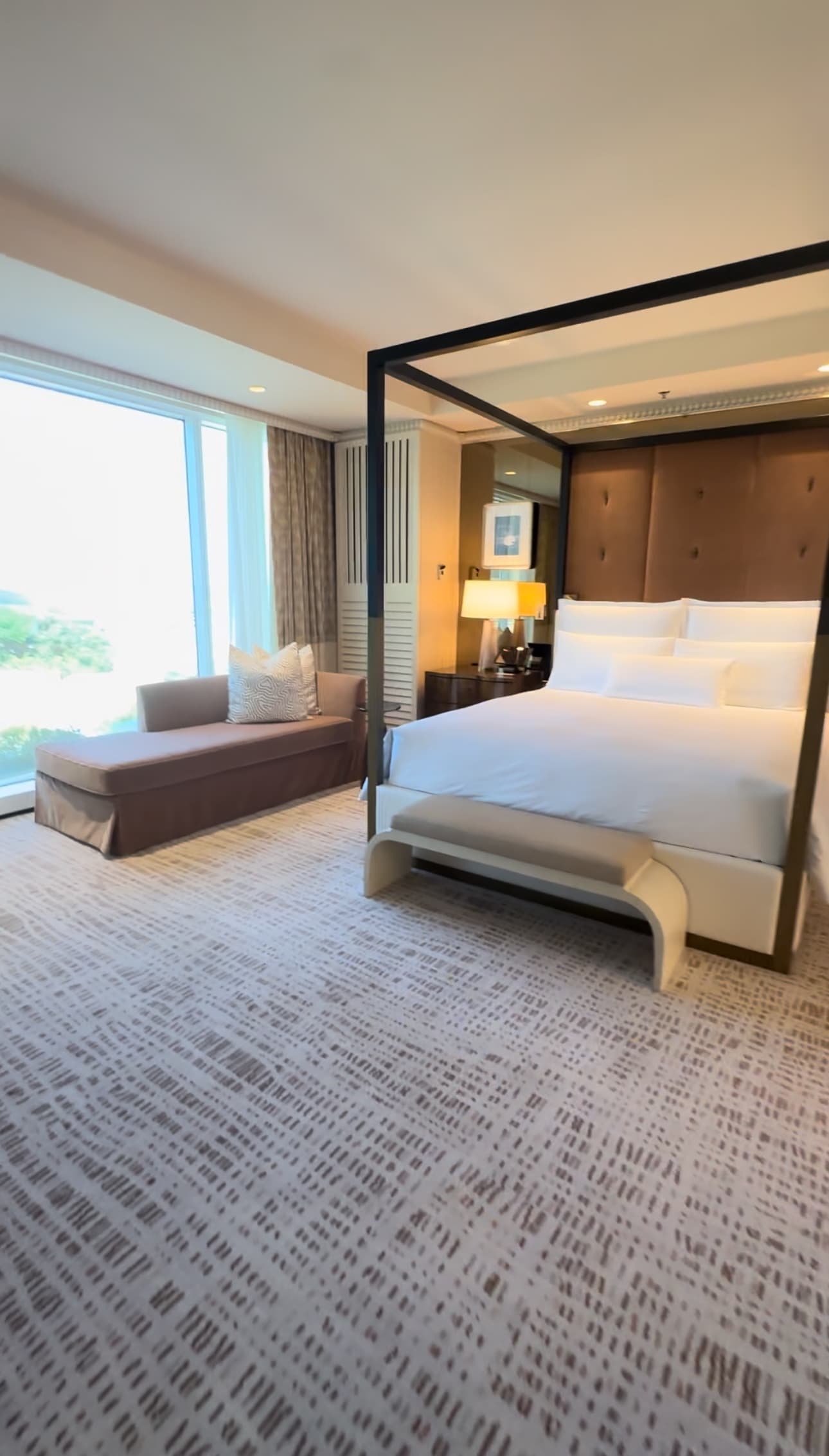 A master bedroom with a large bed and framed canopy, and day bed against the floor-ceiling window.