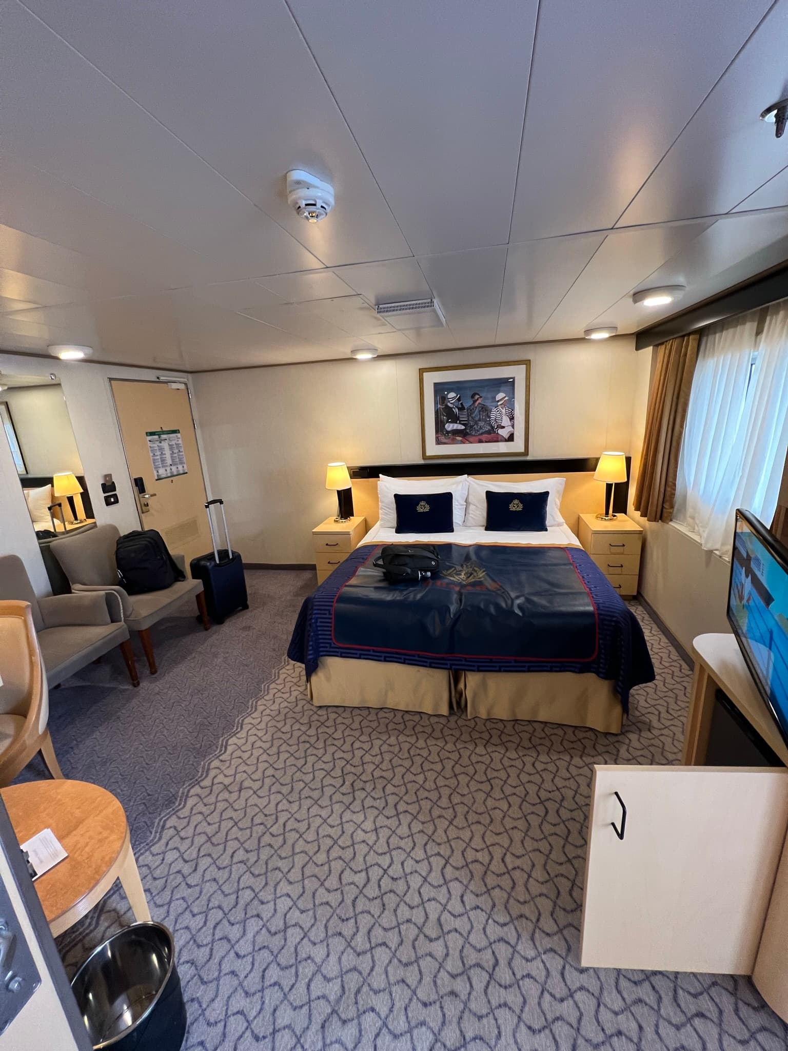 Inside a double room of the cruise ship, with the double bed, soft chairs, small table and television.