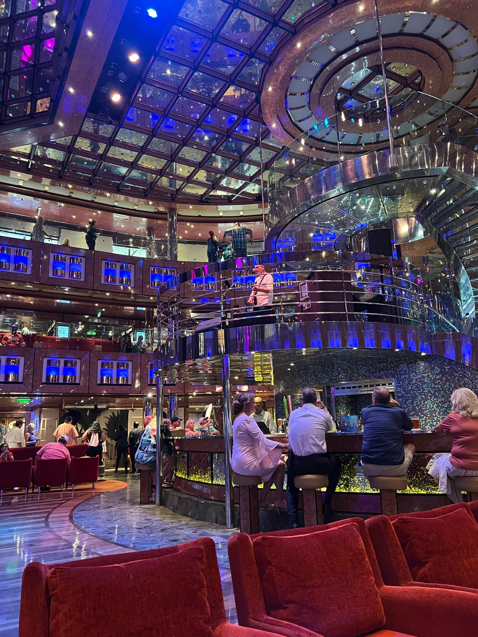 The interior of a cruise ship with aa bar in the middle and blue and purple lighting throughout