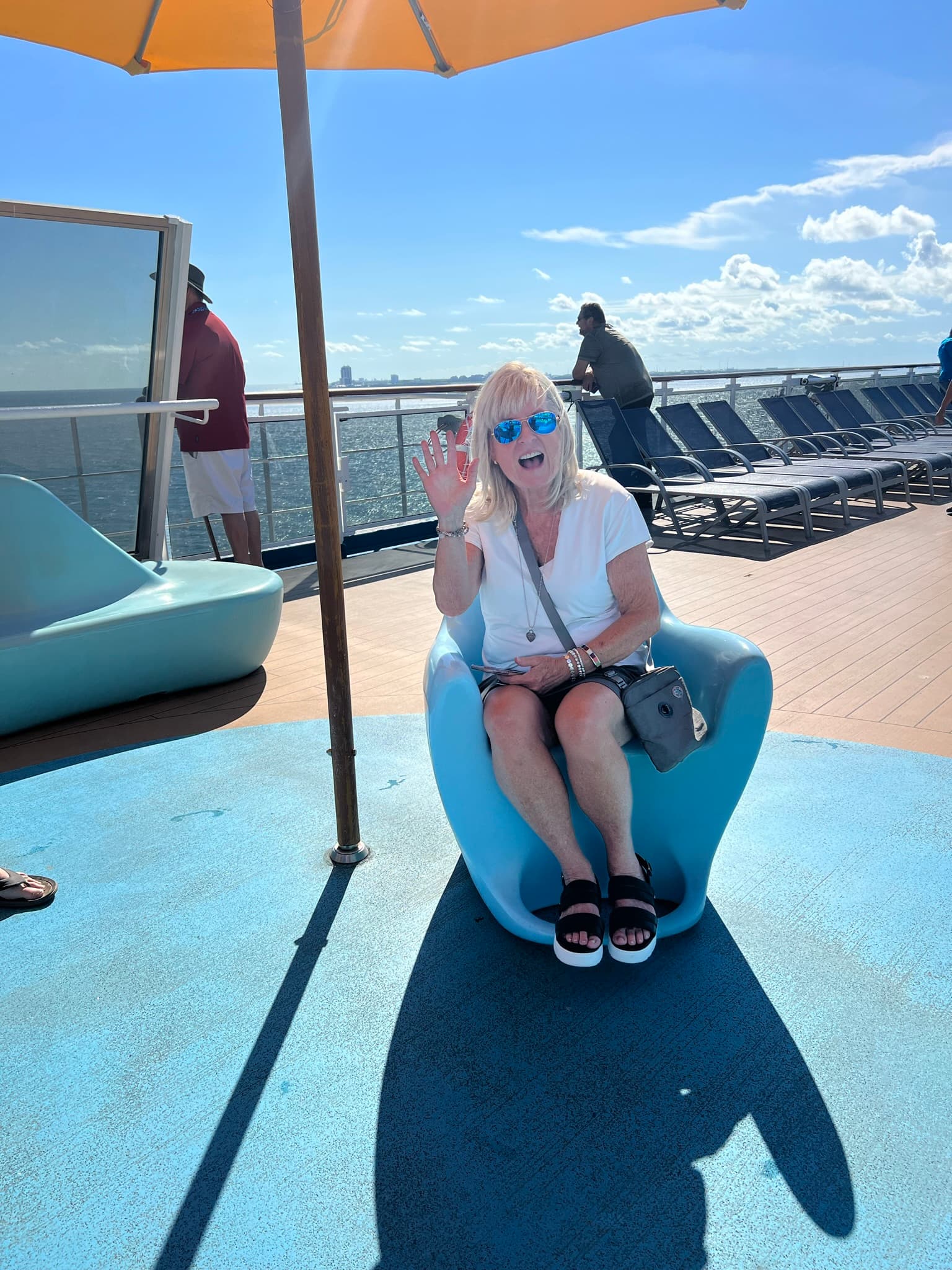 A person sitting in a blue chair on a cruise ship deck smiling for a photo