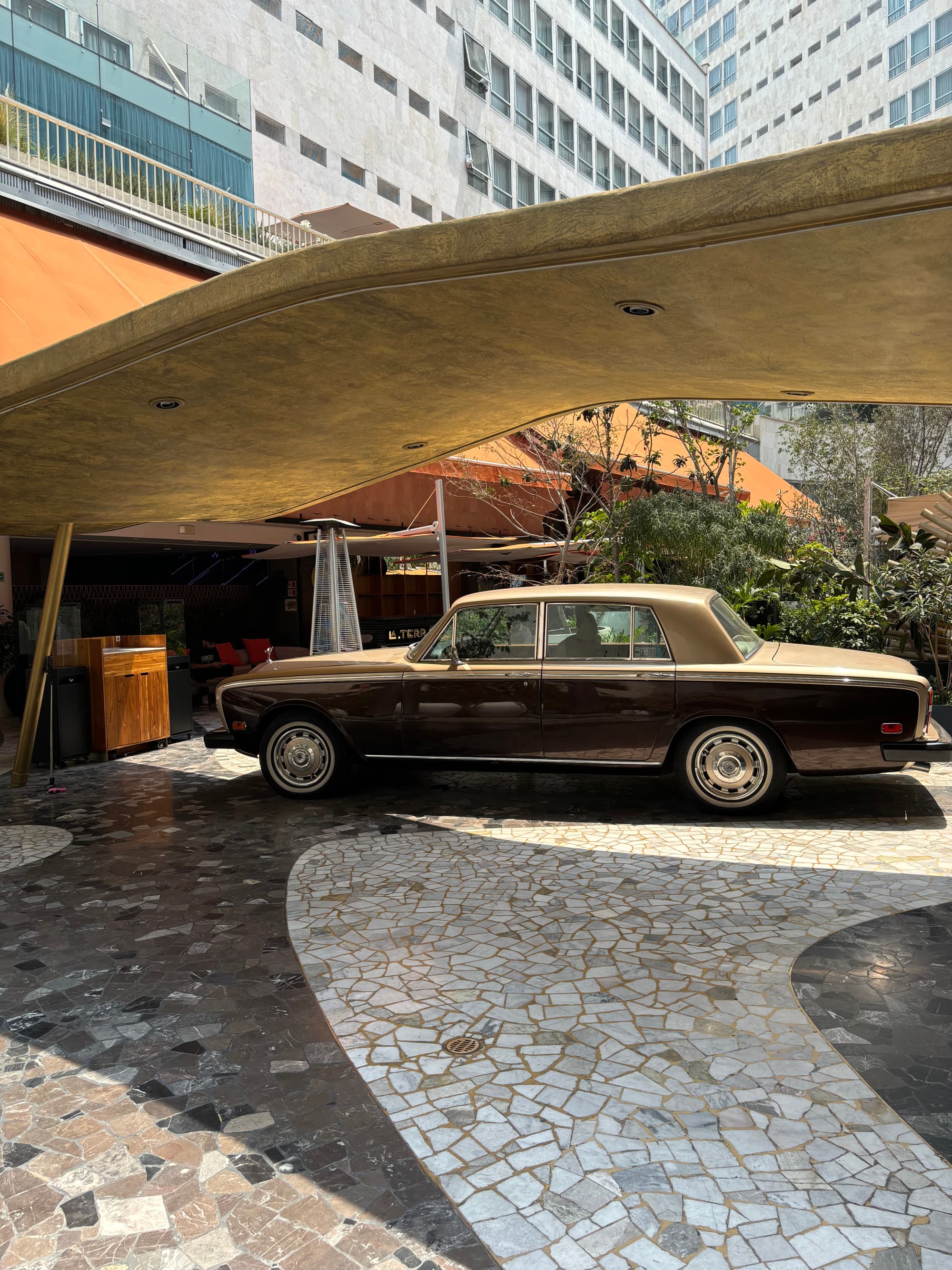 A brown, shiny, antique car elegantly parked before the hotel and underneath a stone awning.