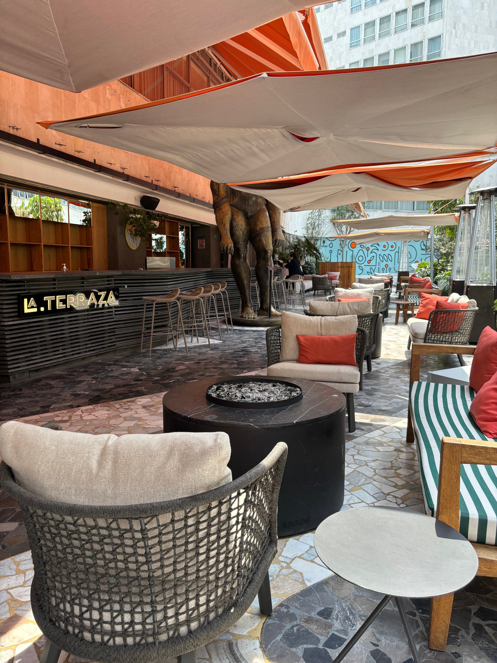 An outdoor lounge area, covered in tented awnings, boho-chic style furniture and fire pits.