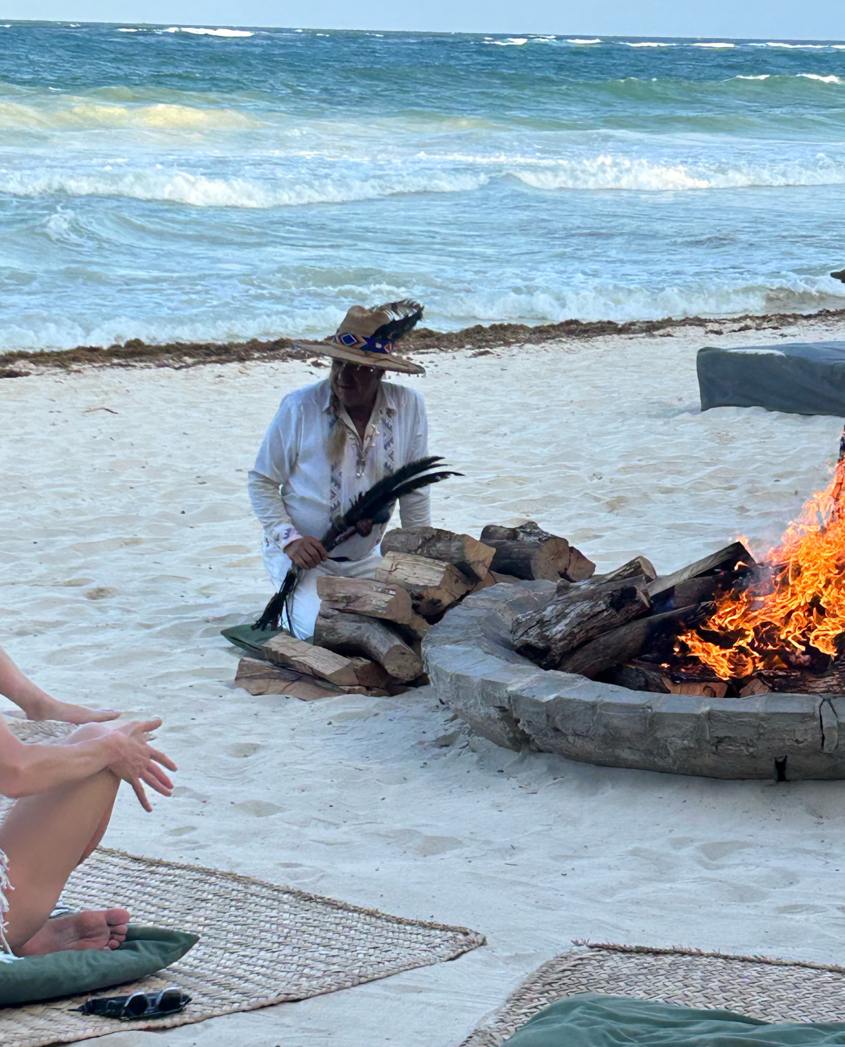 A man conducting a fire ceremony with a round fire pit on the beach