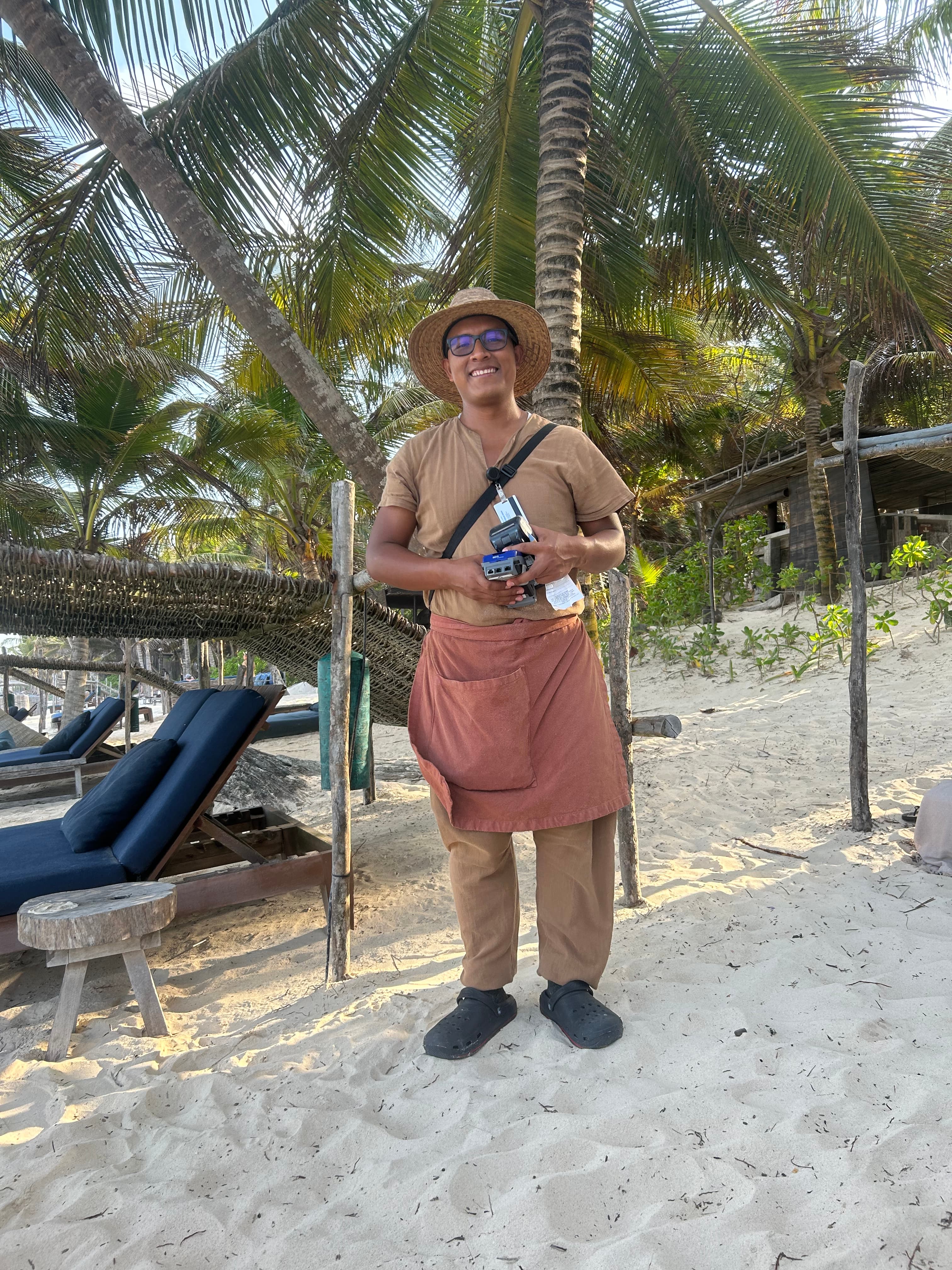 A server in a beige outfit and apron standing on the beach