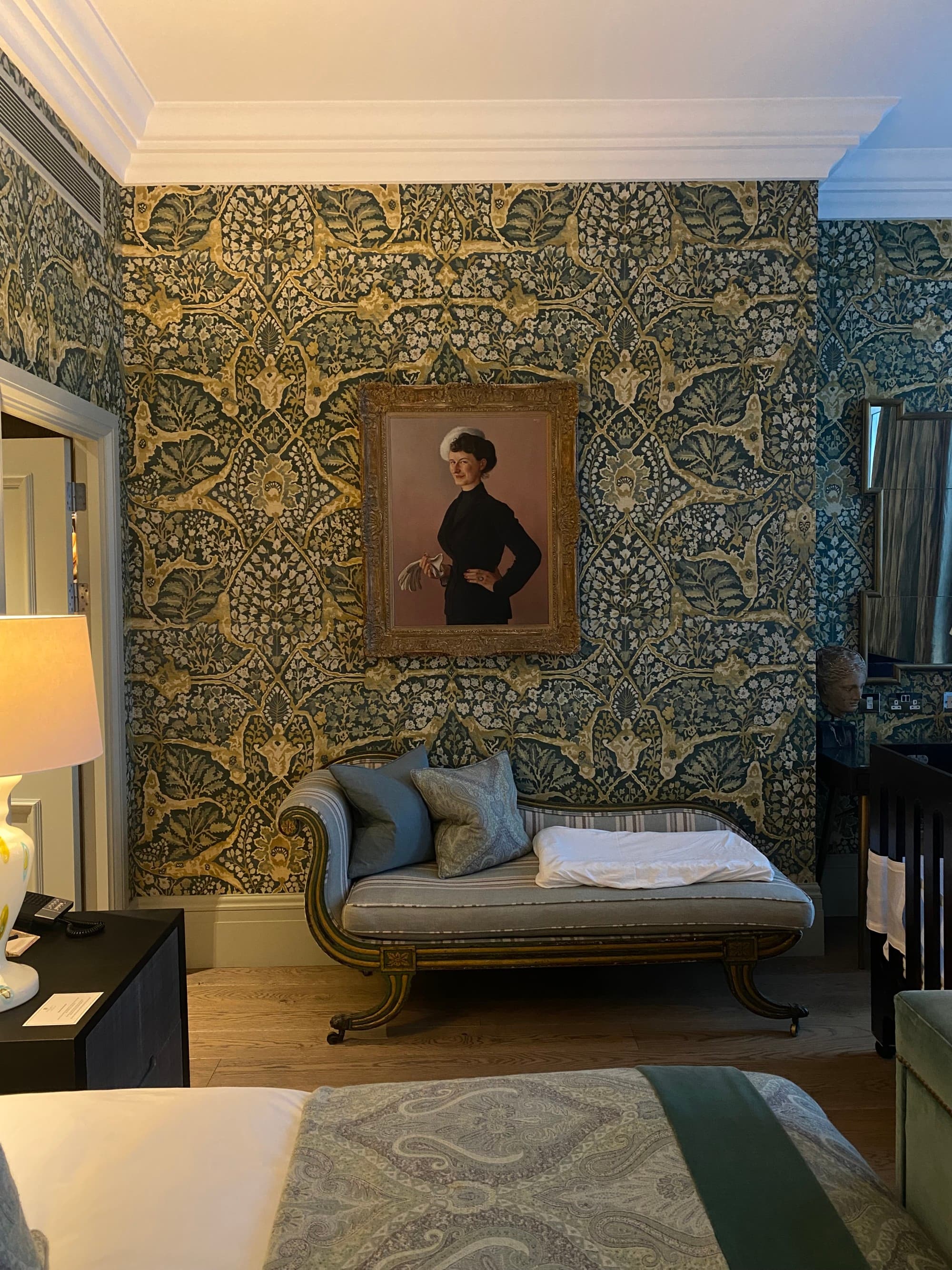 A photo inside one of the hotel rooms with ornate green and gold wallpaper and a chaiselounge against the wall.