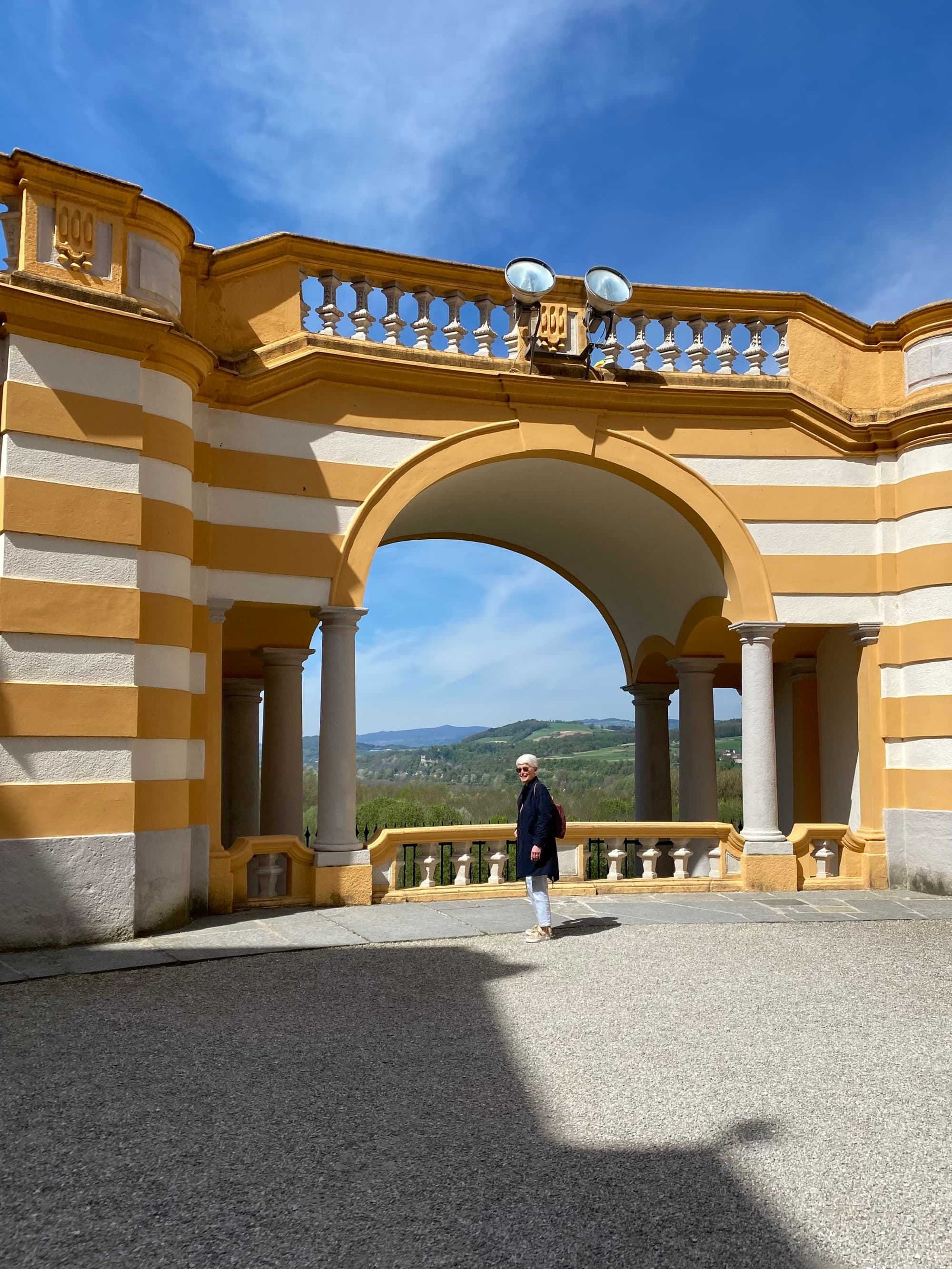 A person standing underneath the archway in an outdoor courtyard of Melk Abbey on a sunny day.