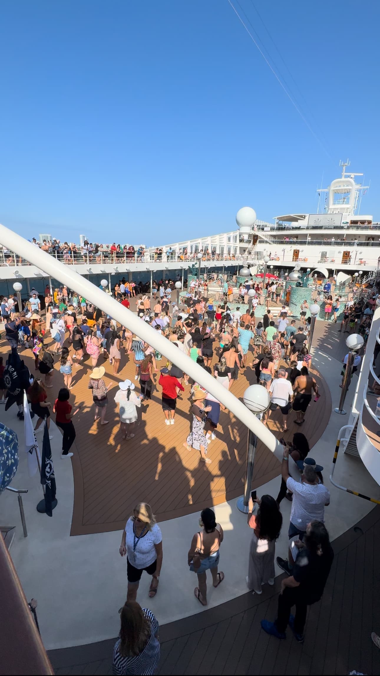 The deck of a cruise ship full of passengers, being welcomed aboard on a sunny day.