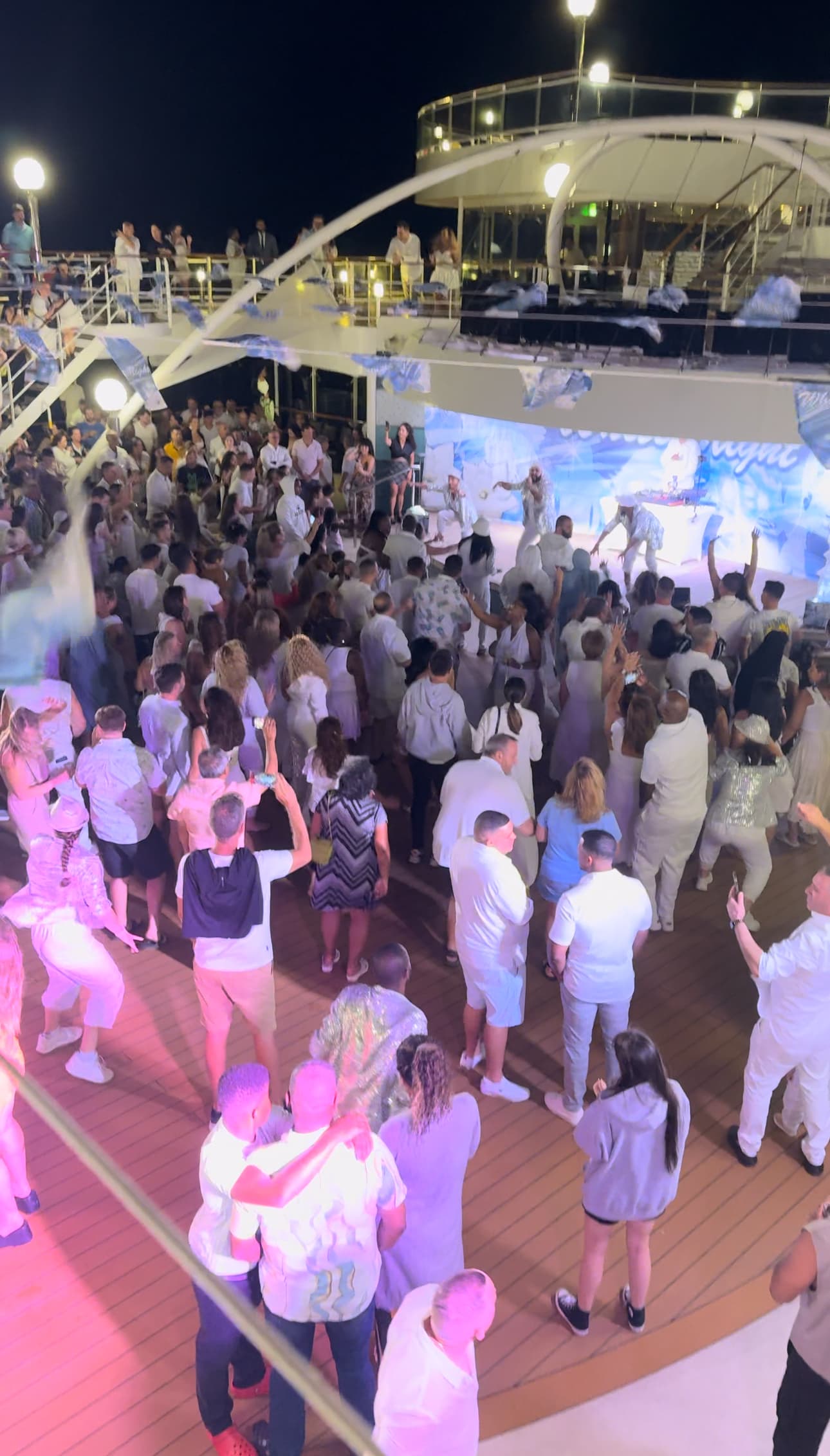 An audience dressed in white viewing a performance on an outdoor deck of the cruise ship at night.