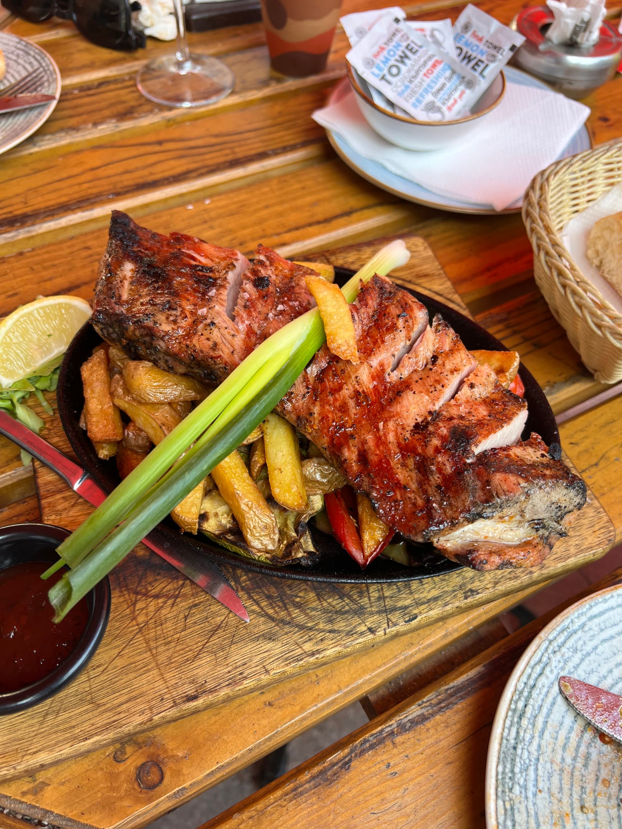 This image depicts meat and vegetables on a platter placed on top of a wooden table with other various plates in the surrounding area.