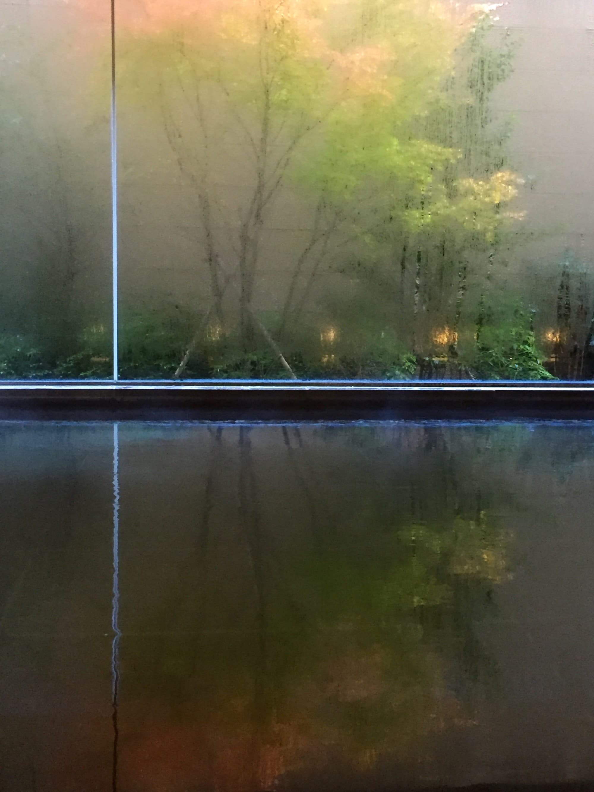 A view of the hot spring (onsen) at the Hyatt Regency Hakone, with steamed window and trees outside with orange and green leaves