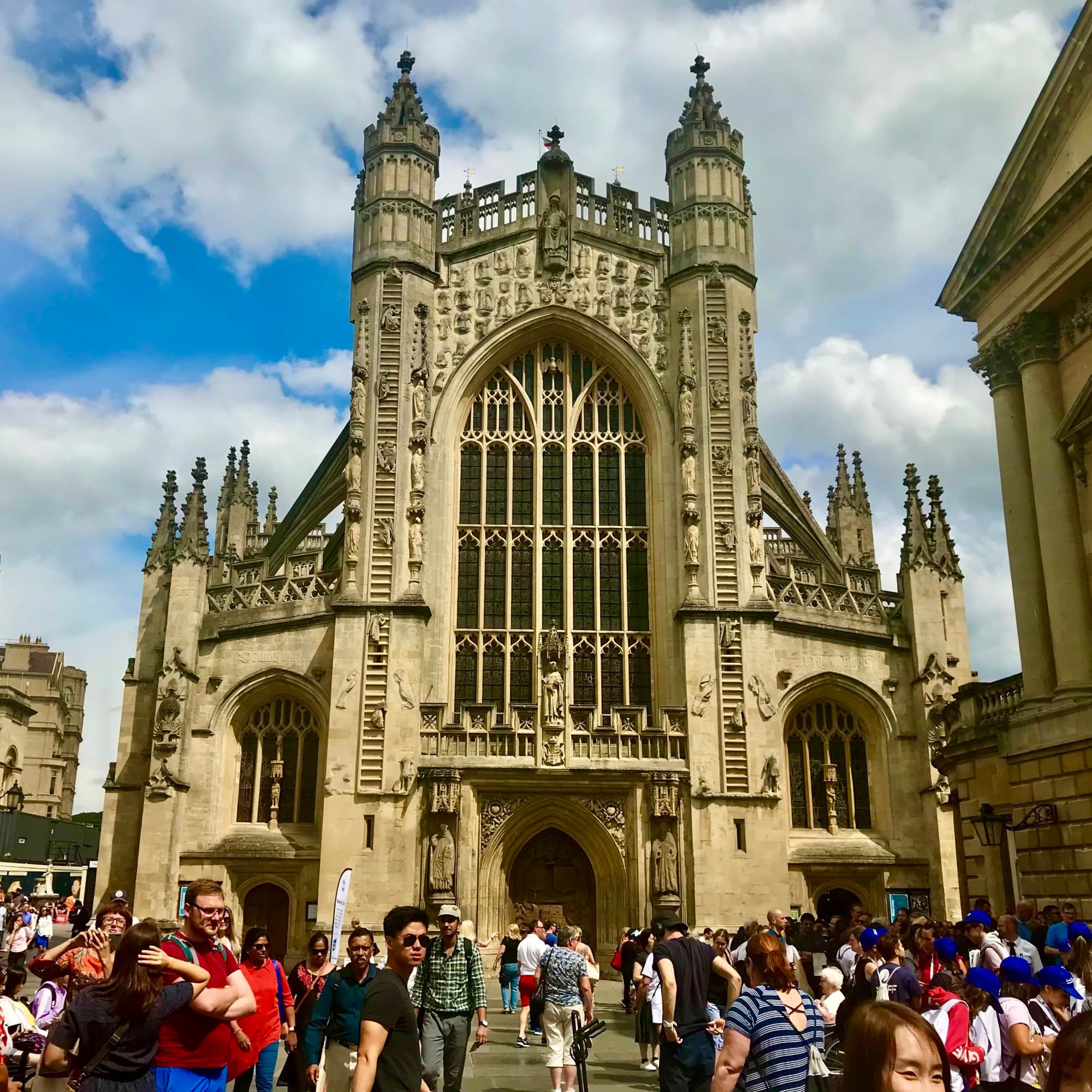 A view of the elaborate Bath Abbey with lots of tourists walking around in front of it.