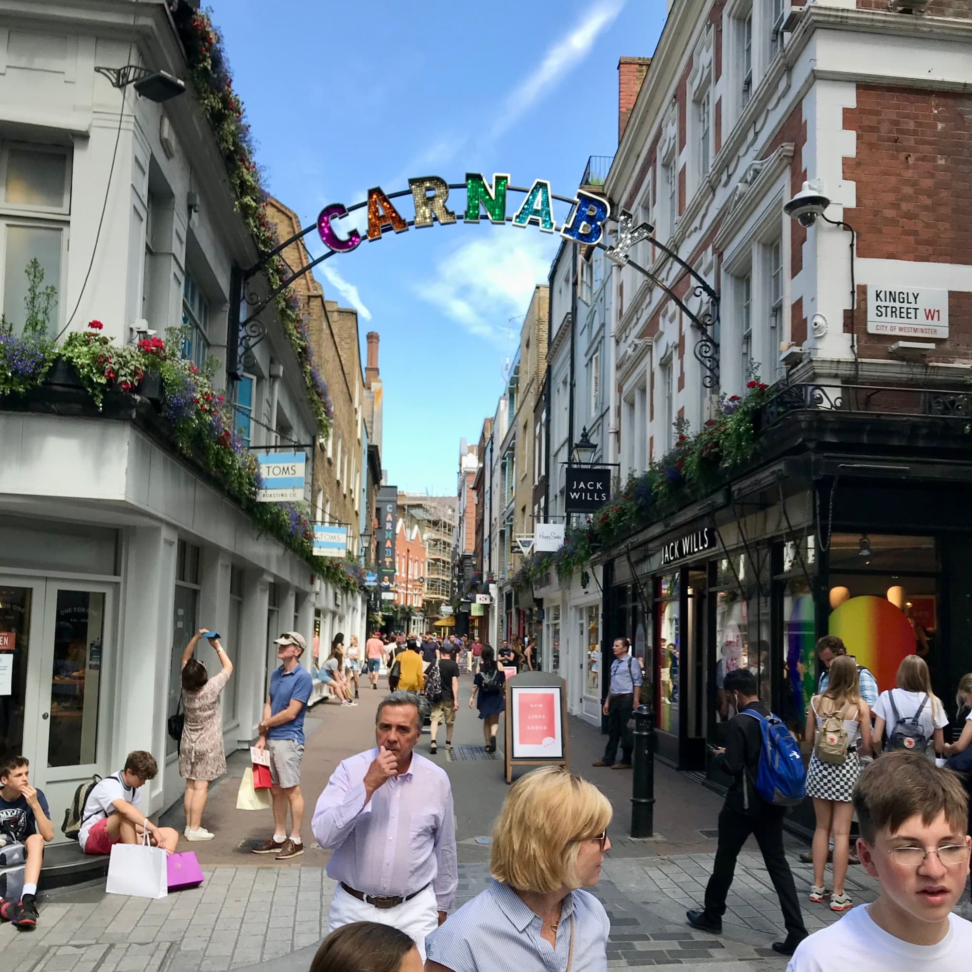 A view of people walking around Carnaby Street with an arch displaying colorful letters of the location.