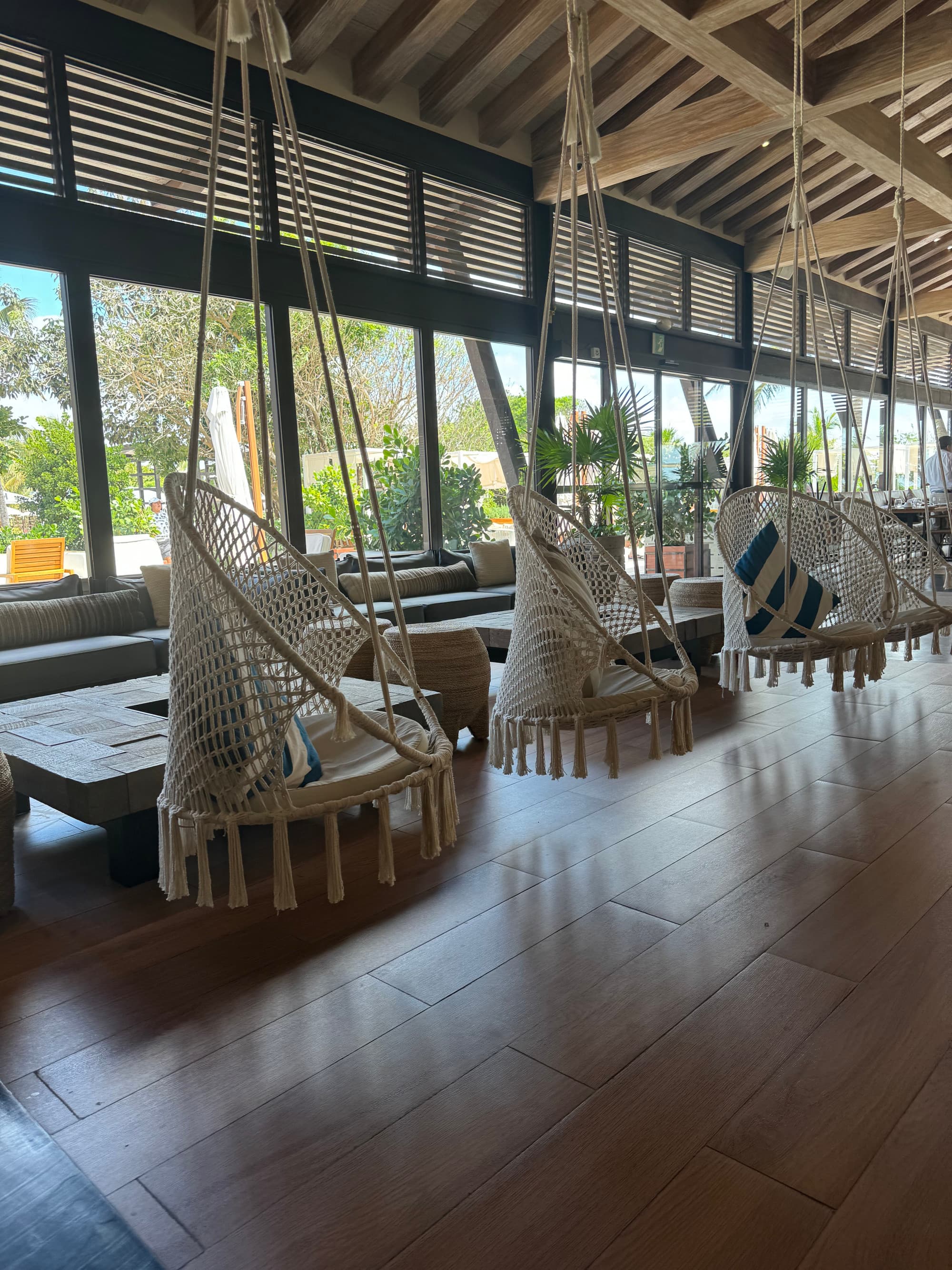 Swinging wicker chairs hanging from wooden panels on a ceiling with a couch and lounge seating in the background.