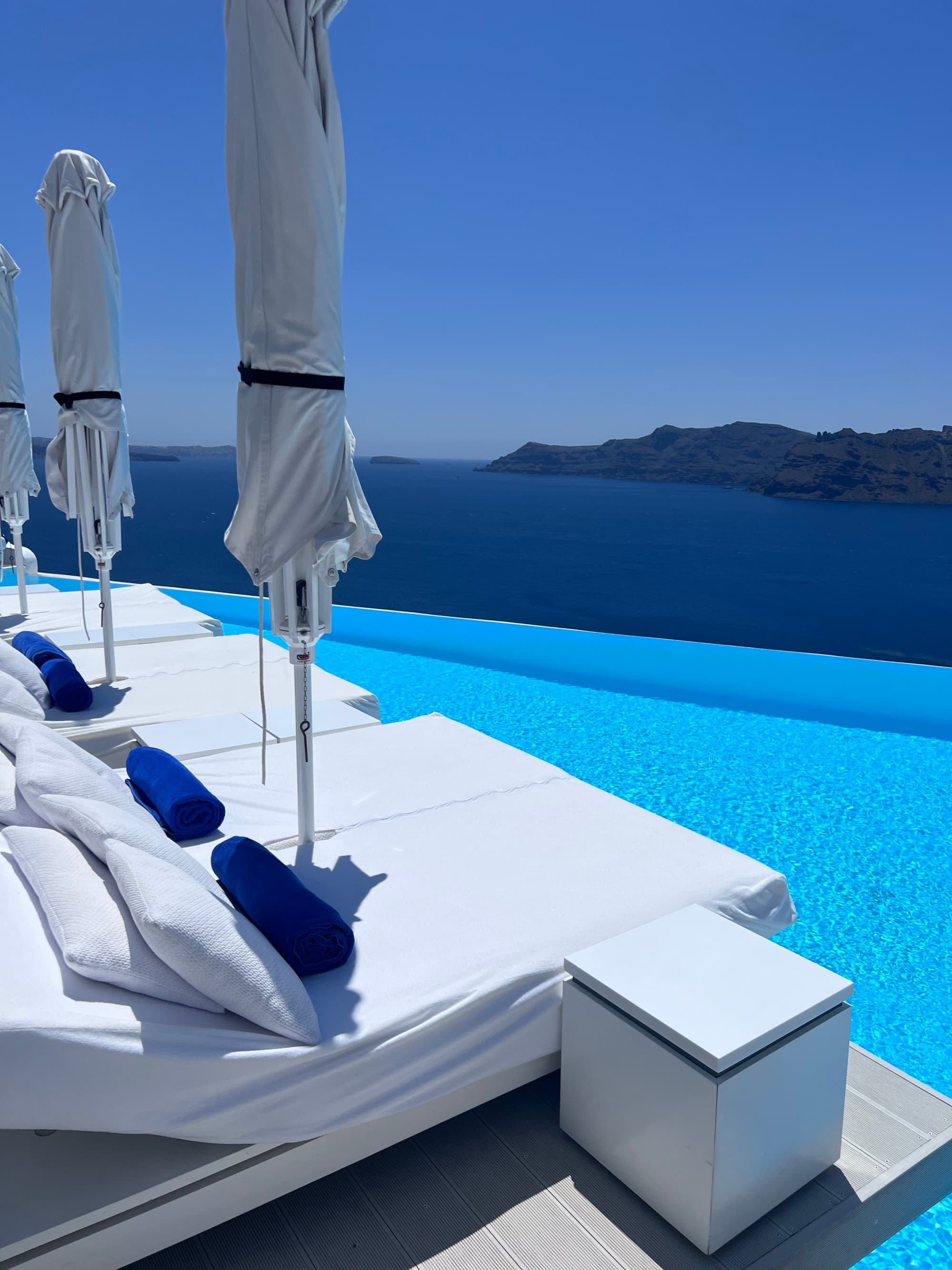 white loungers beside a blue cliffside infinity pool