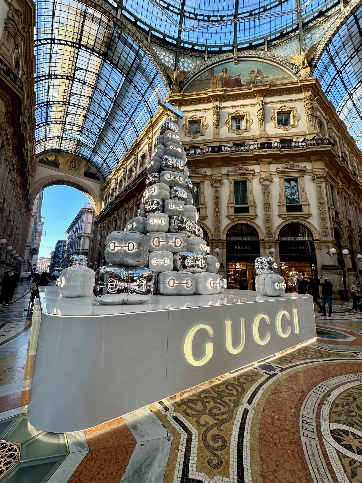 A low-angled photo of large Gucci display inside a building with glass ceilings