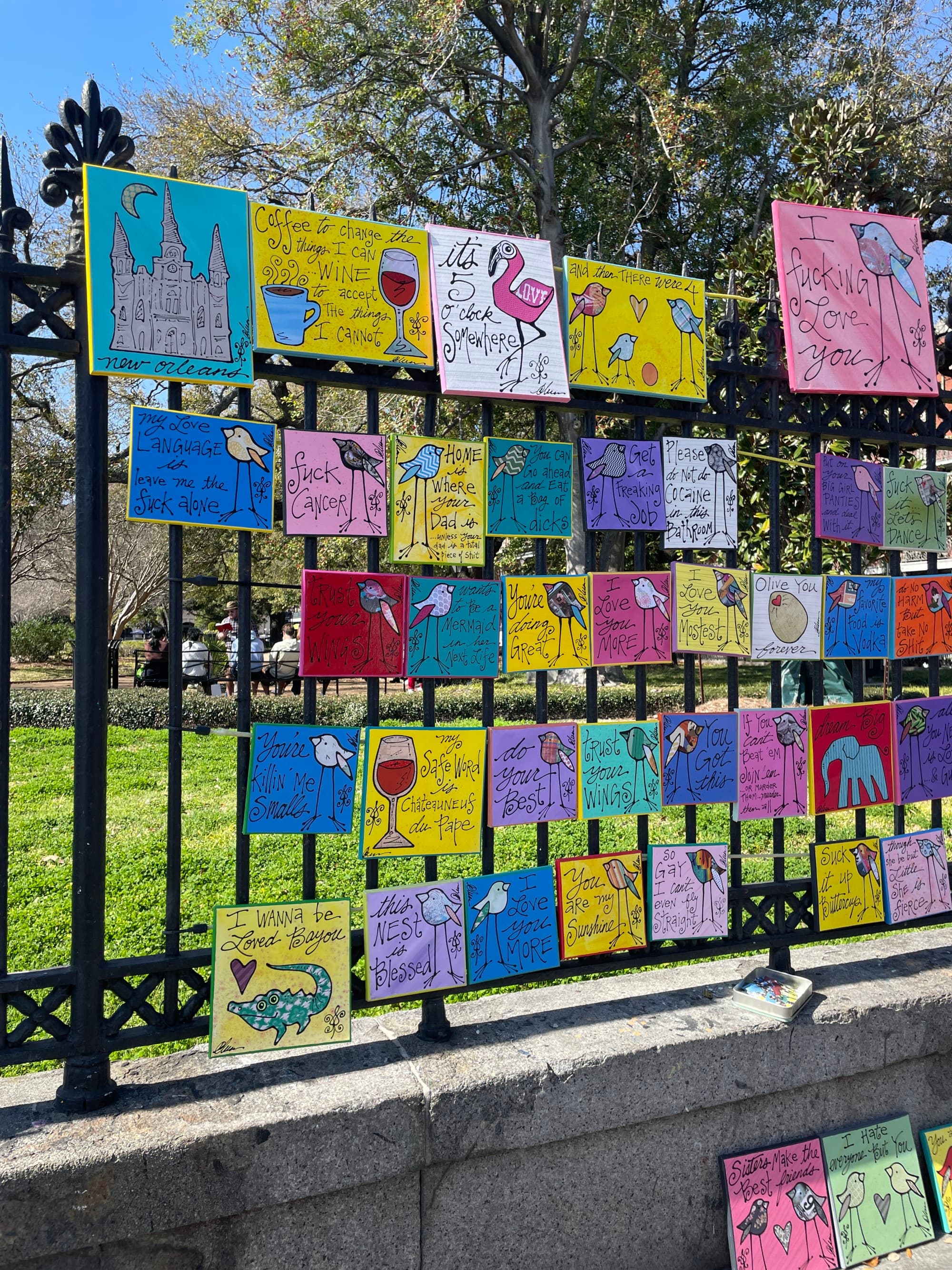 A view of colorful cards hanging on a metal fence outside.