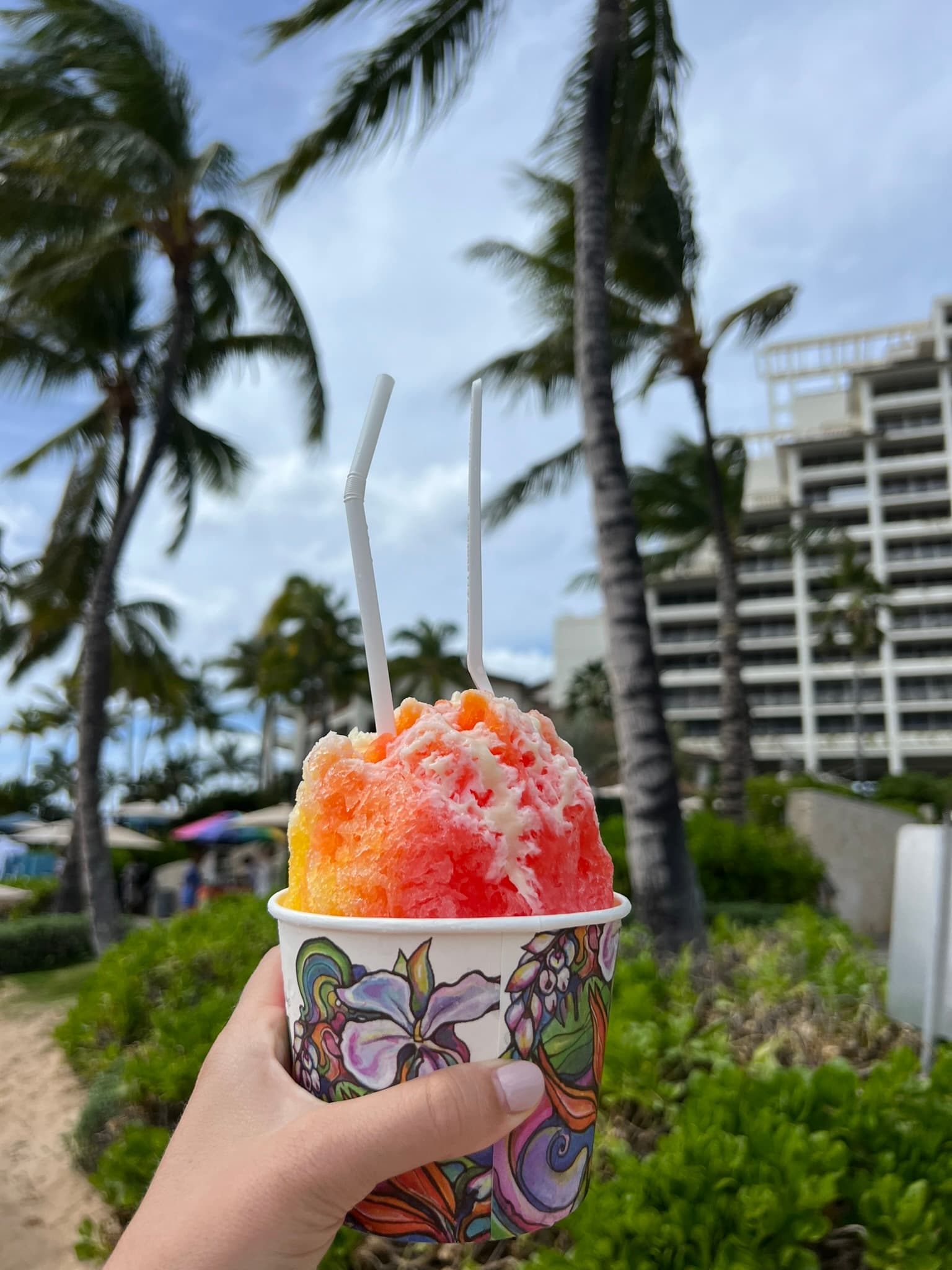 A hand holding up a cup of red and yellow shaved ice