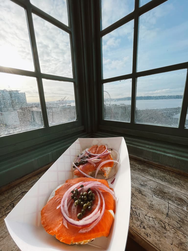 Bagels and lox in a paper bowl in front of corner windows