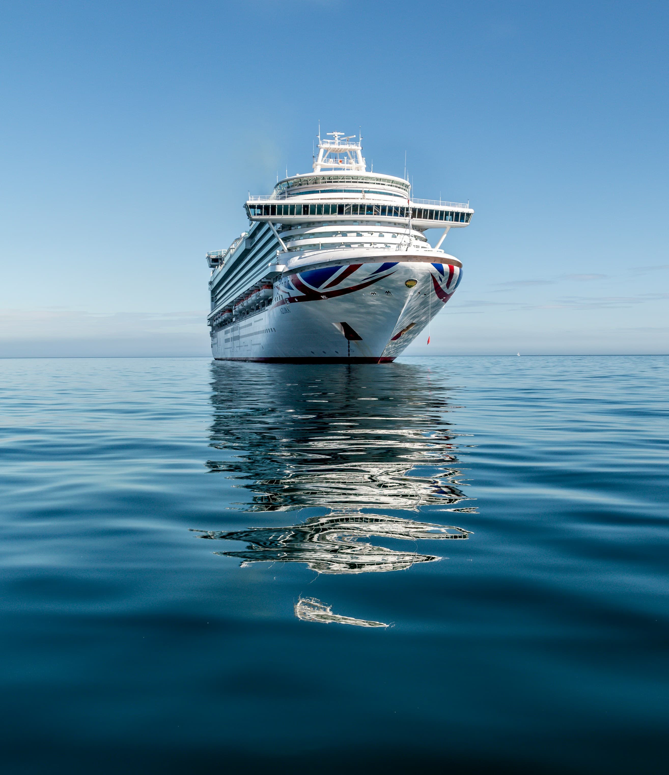 An image of a cruise ship sailing through calm, blue water on a sunny day.