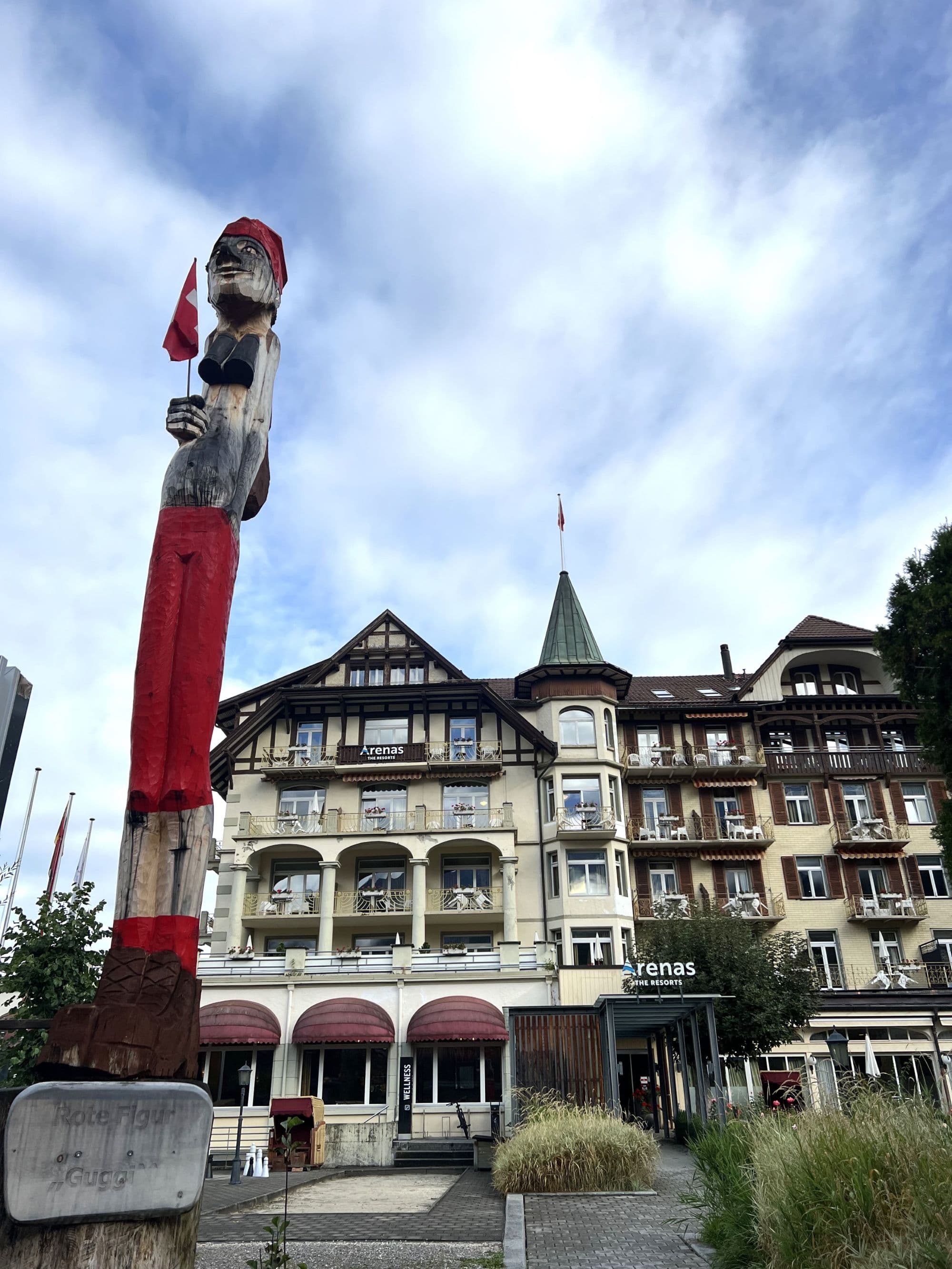 A view of the outside of the hotel building, and a large statue of a figure holding a Swiss flag.