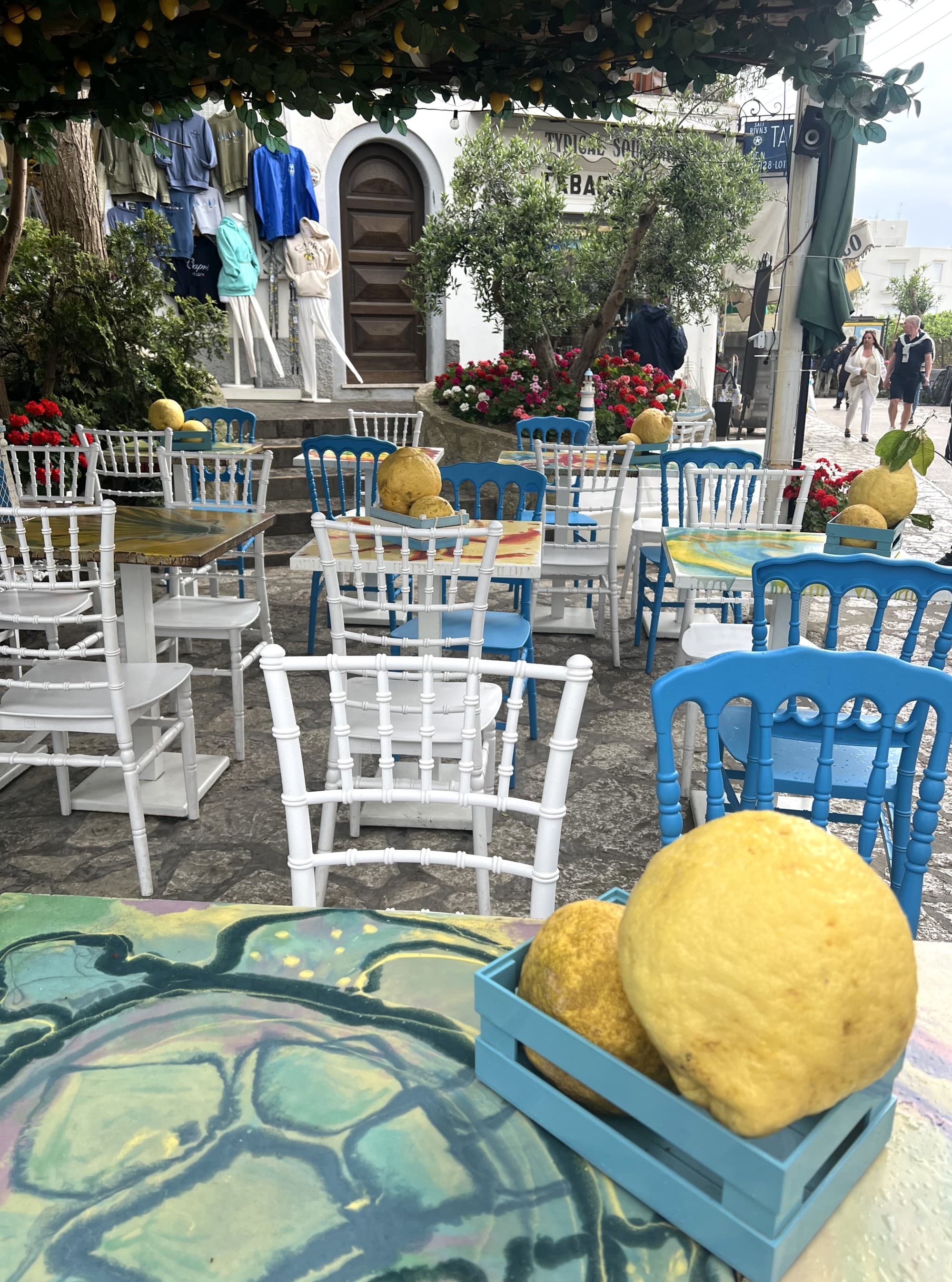 Restaurant patio with blue and white wooden chairs and a bowl of lemons in the foreground