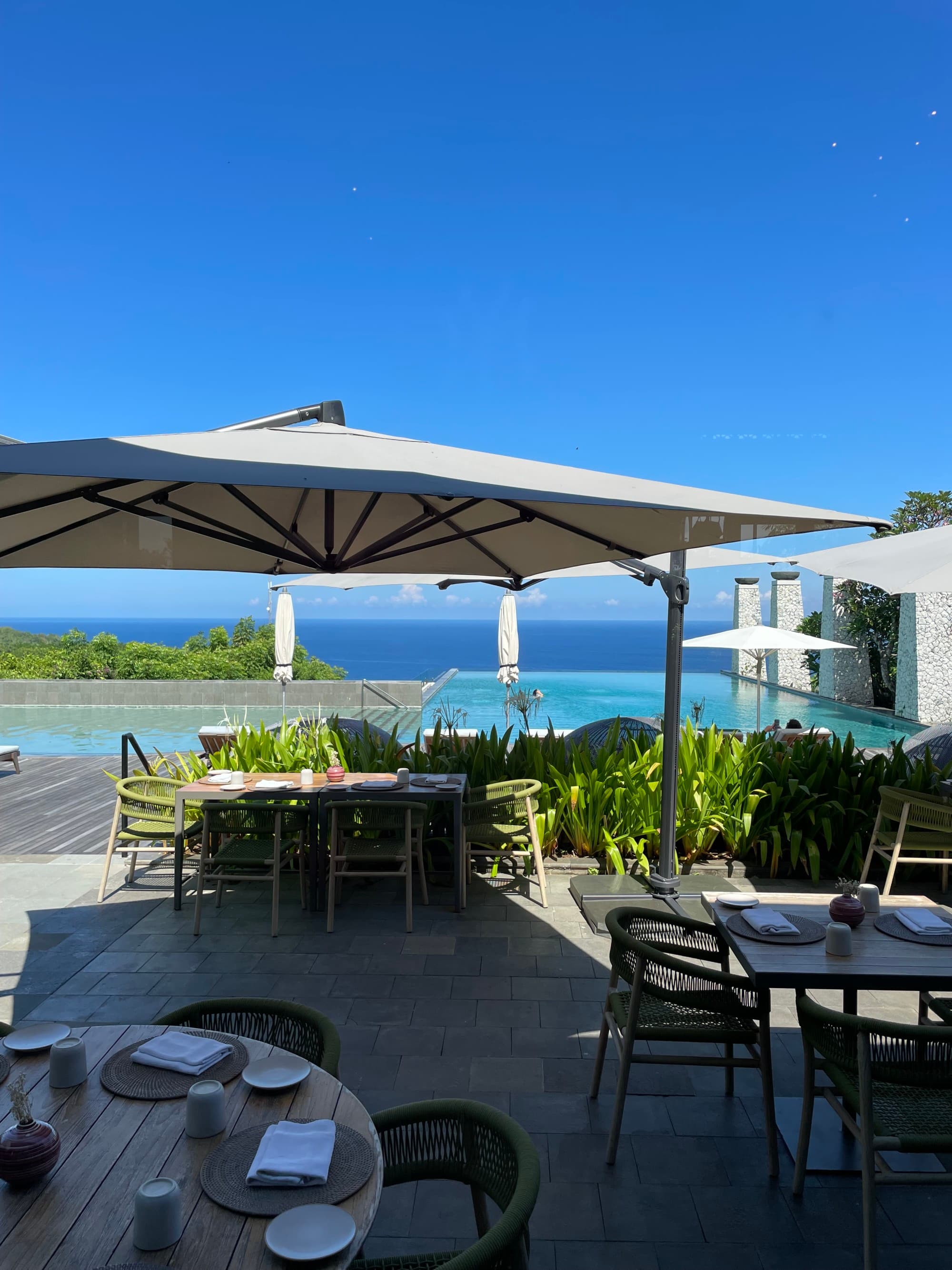 An outdoor seating area with a swimming pool in the background during the daytime