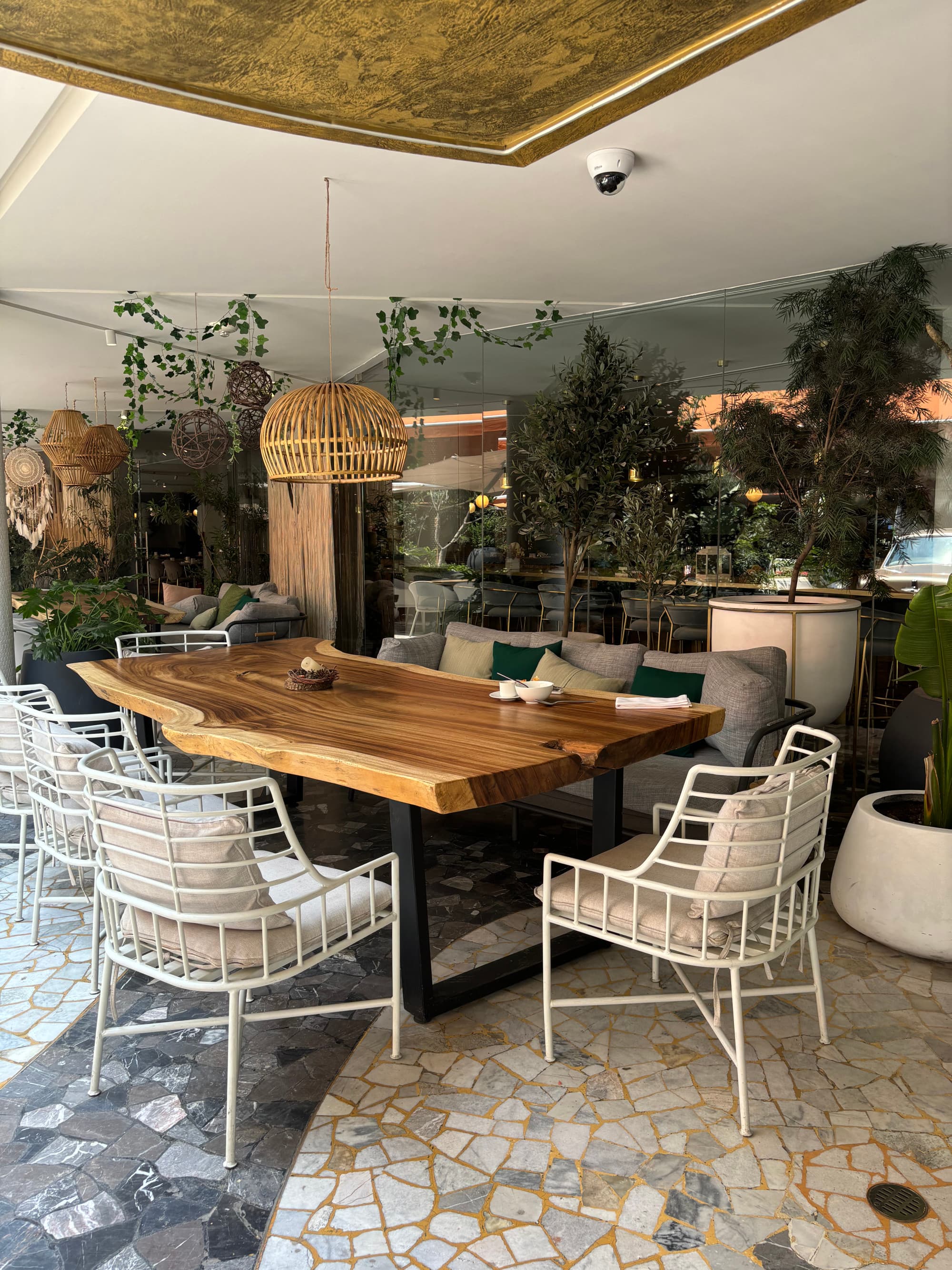 The dining area of the hotel with a large, wooden table, white, metal chairs, and a gray couch.