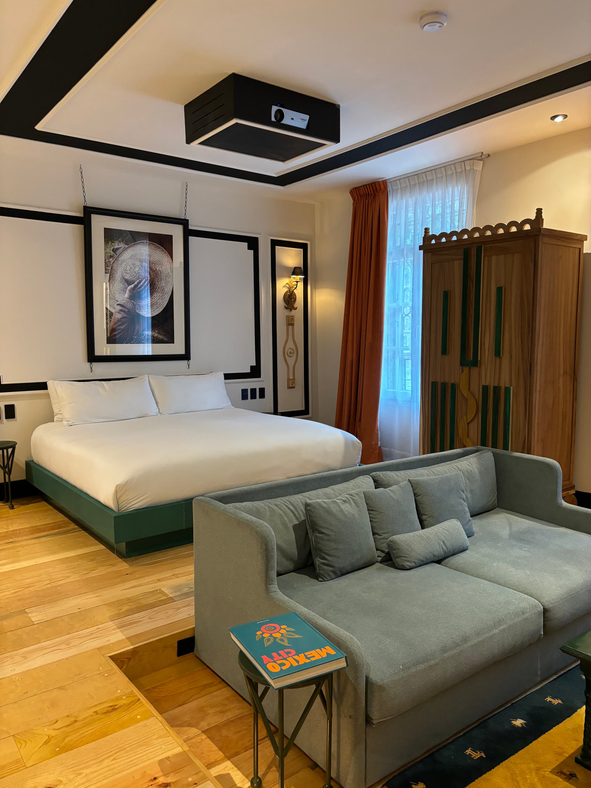 A hotel room with a white bed and gray couch in the center